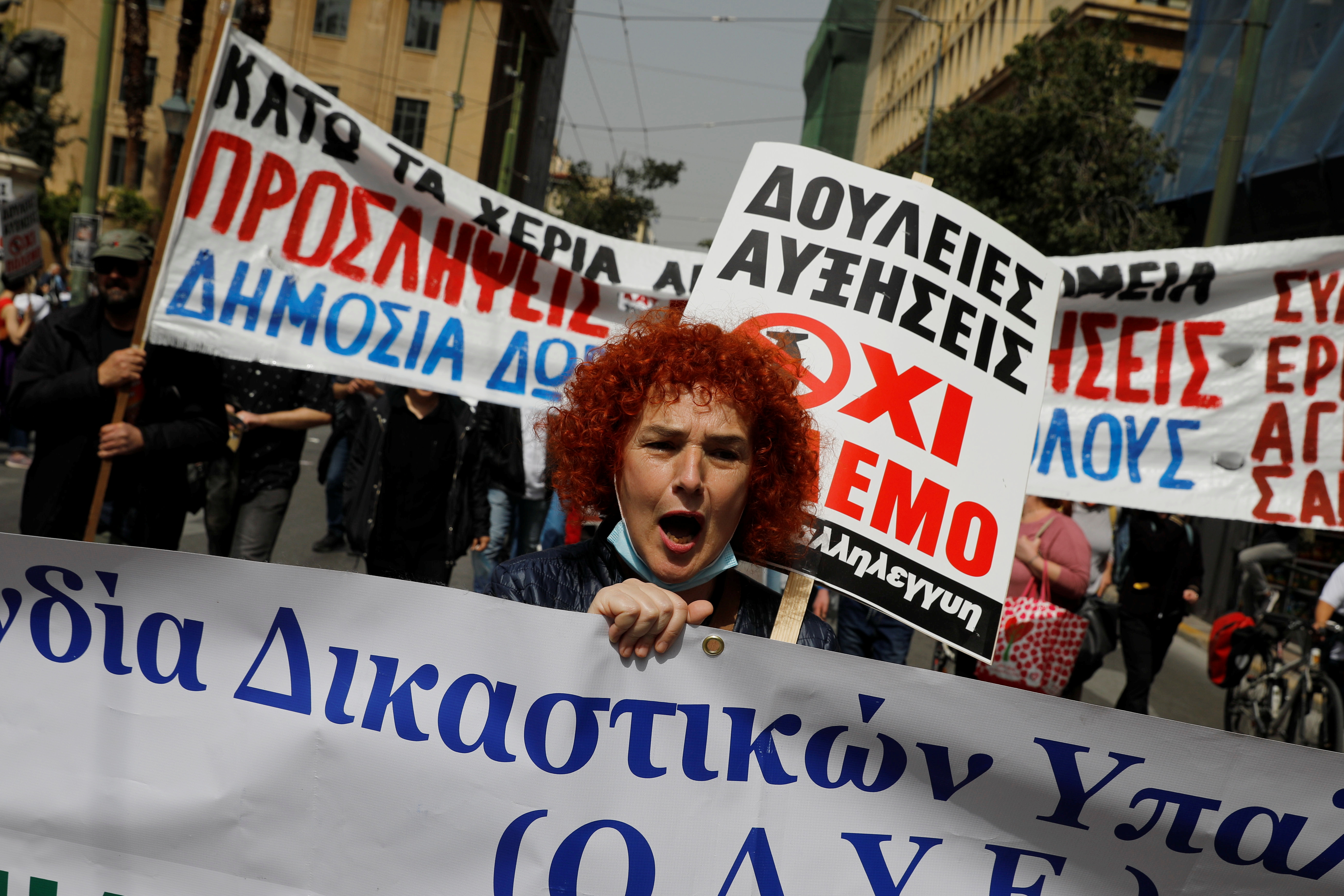 A woman holds a banner and a sign, while taking part in a protest during a 24-hour strike over high prices and low wages in Athens, Greece