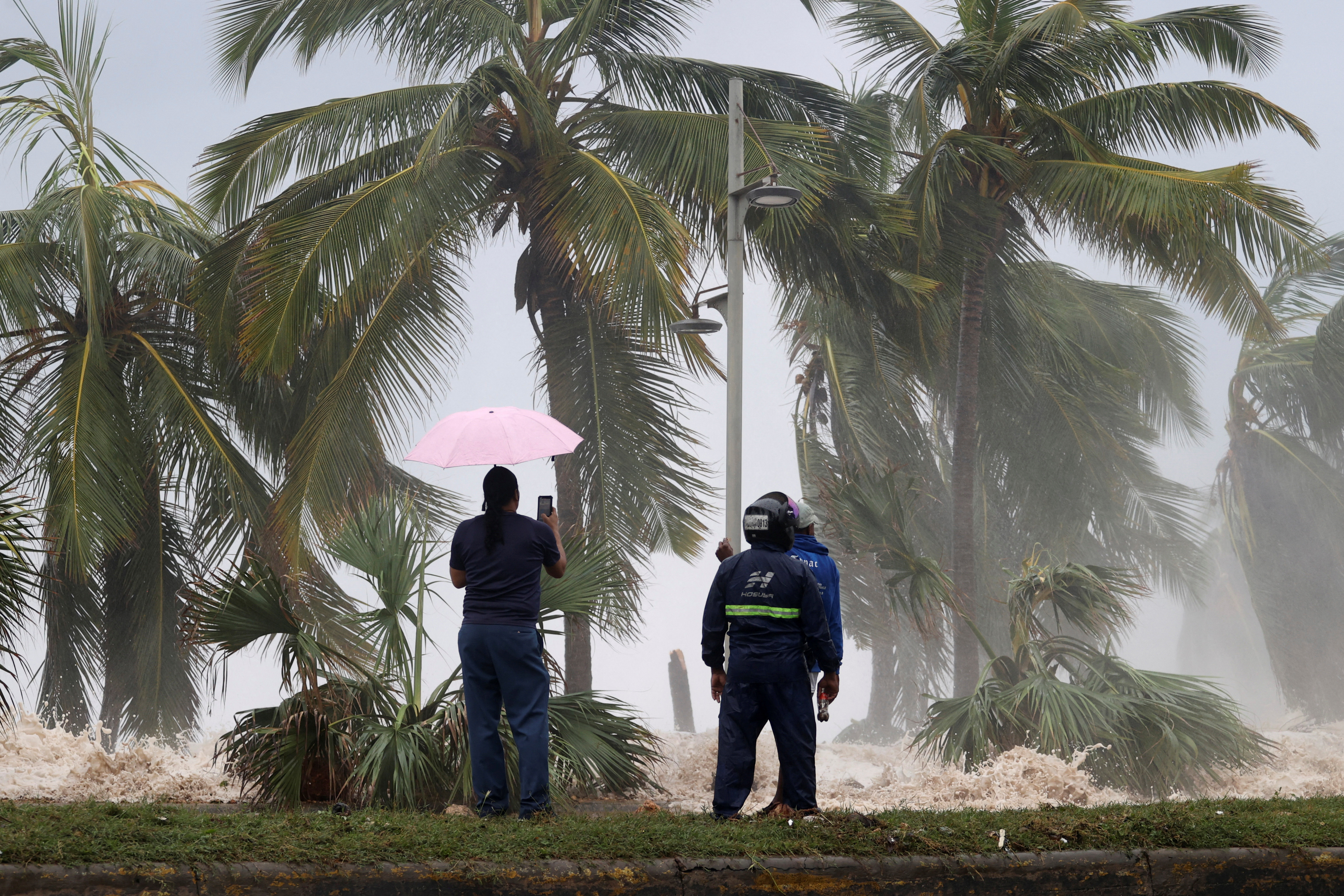 People stand in front of waves crashing against the shore as Hurricane Beryl moves south of the island, in Santo Domingo, Dominican Republic
