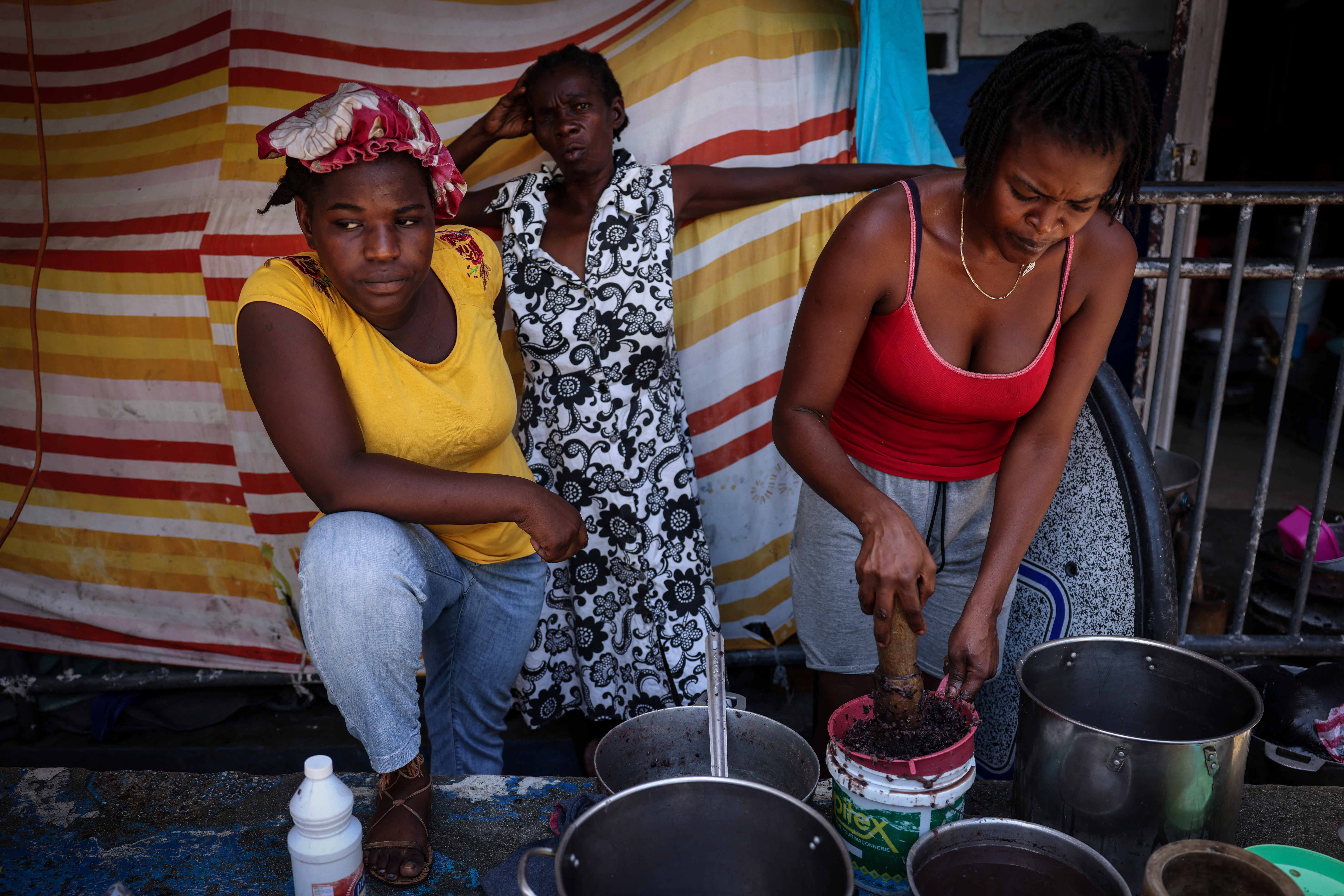 Women displaced by gang violence in Haiti stand outside tents in a camp for internally displaced persons