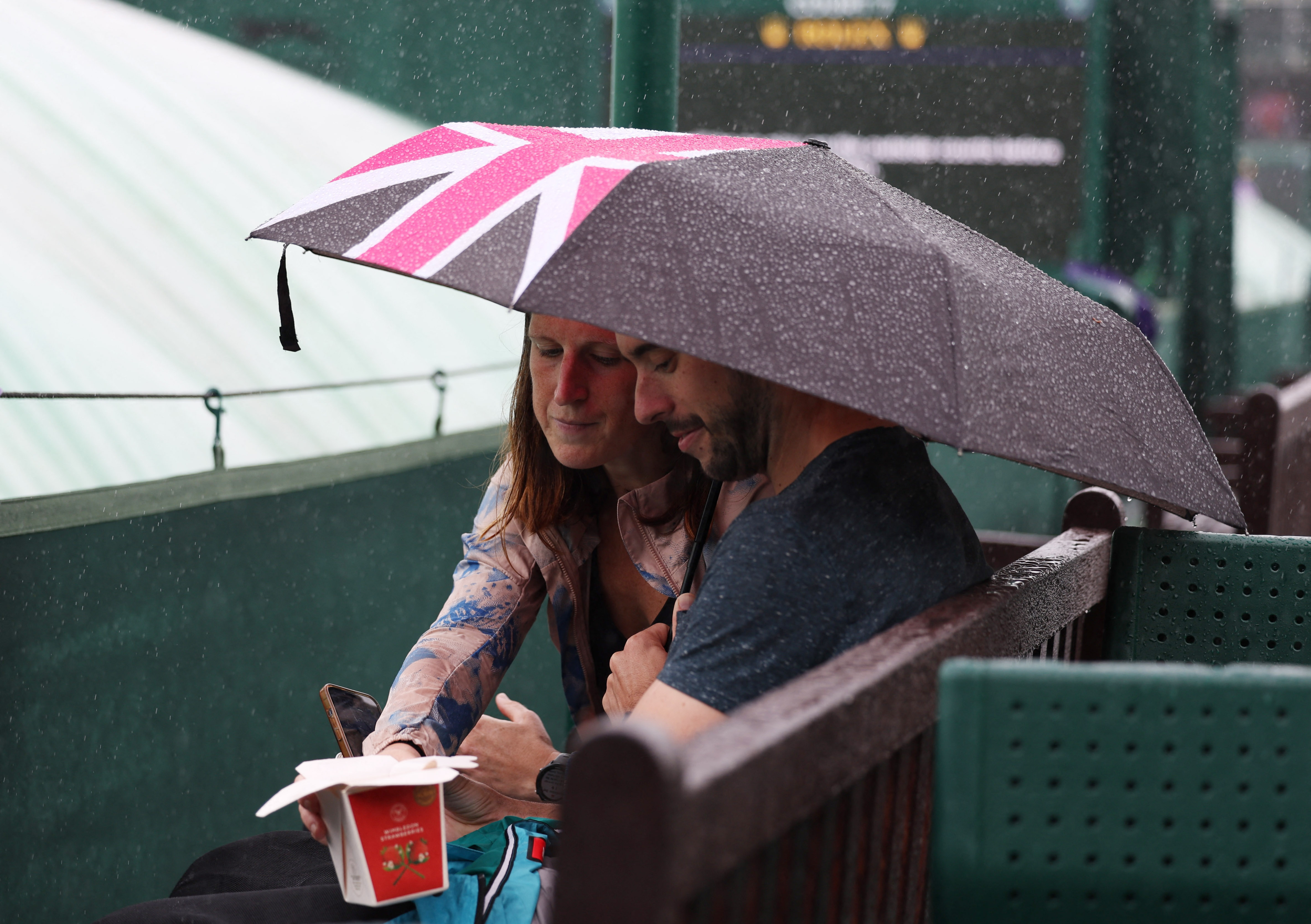 Tennis - Wimbledon - All England Lawn Tennis and Croquet Club, London, Britain - July 5, 2024 Spectators take cover under umbrellas as rain delays play REUTERS/Isabel Infantes