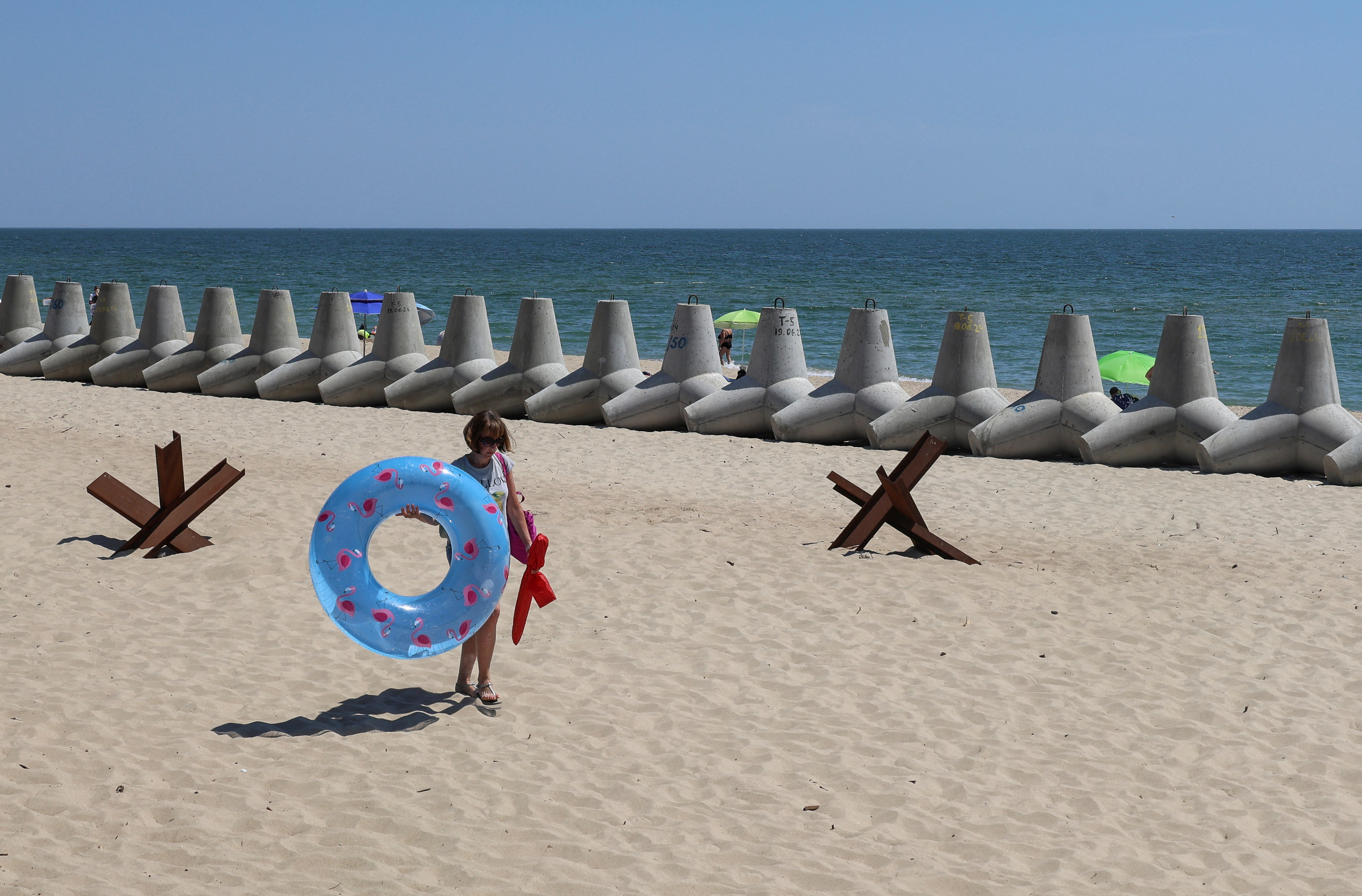 A person carries a swimming ring near tetrapods used as barriers against Russian military landing ships, amid Russia's attack on Ukraine, on the beach in the city of Chornomorsk, Odesa region, Ukraine July 9, 2024. REUTERS/Nina Liashonok
