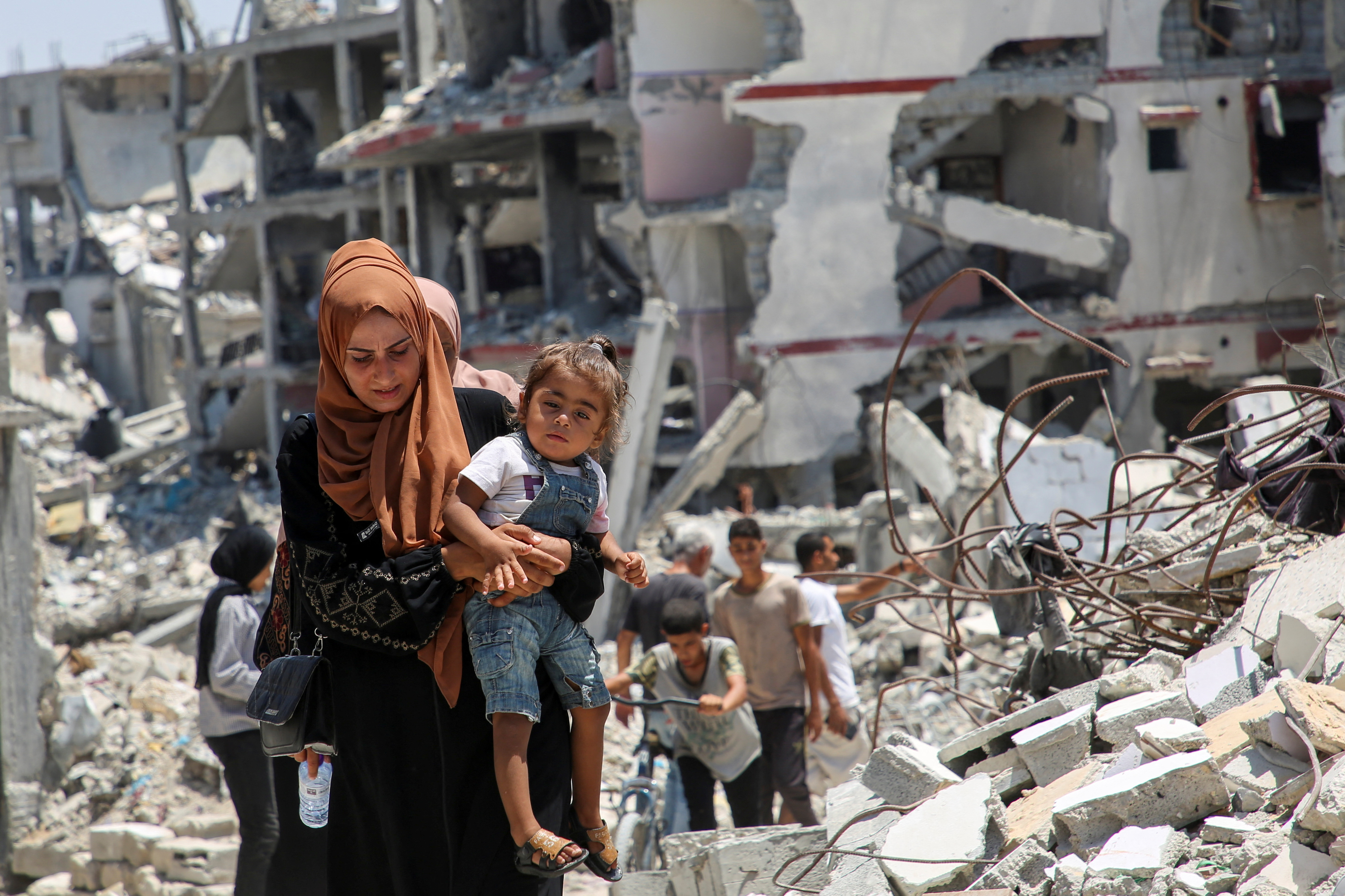 A Palestinian woman holds her daughter as she walks past the rubble of houses