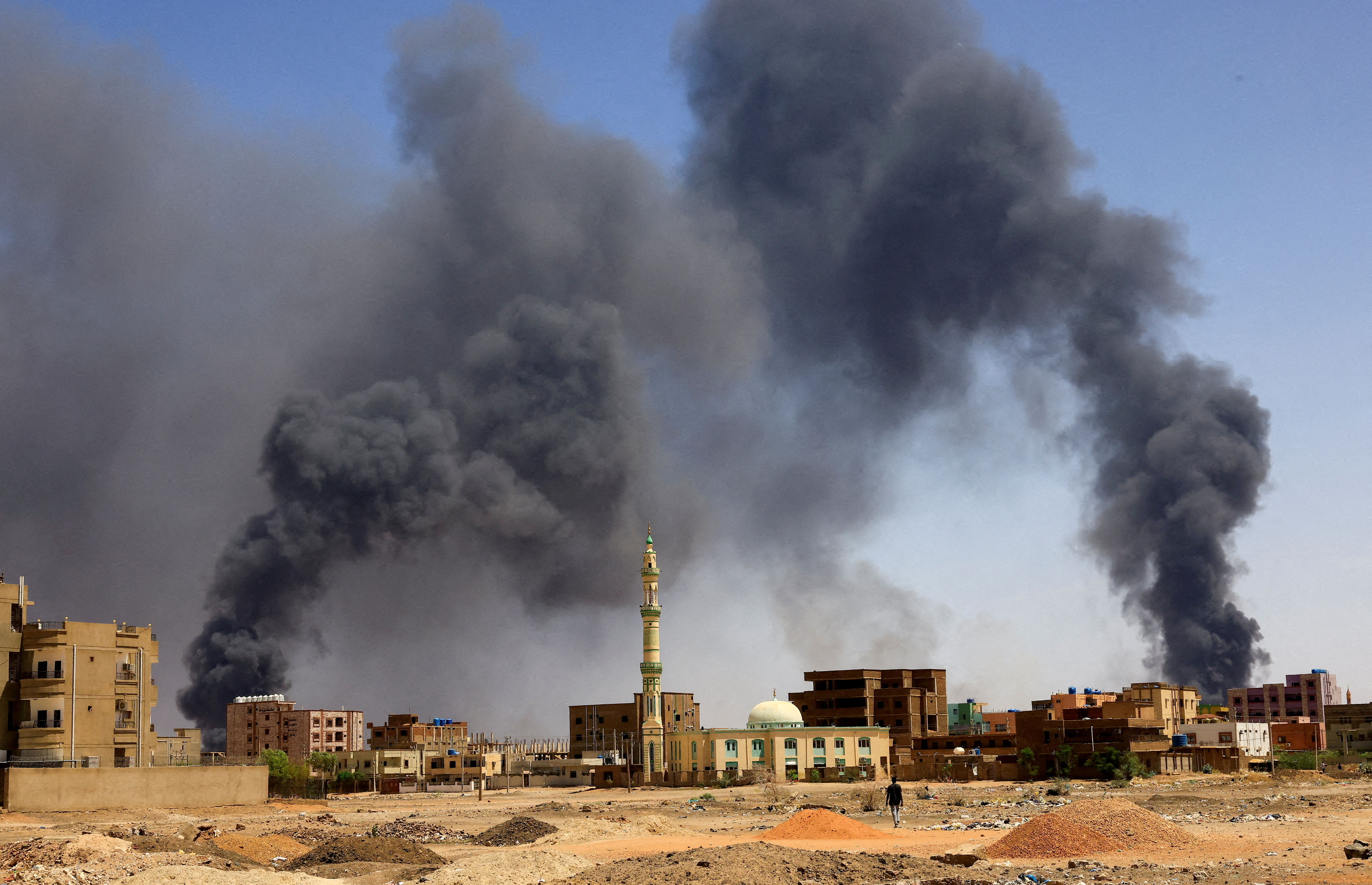 A man walks while smoke rises above buildings after aerial bombardment, during the war between the Rapid Support Forces (RSF) militia and the Sudanese army in Khartoum North, Sudan, May 1, 2023 [Mohamed Nureldin Abdallah/File Photo/Reuters]