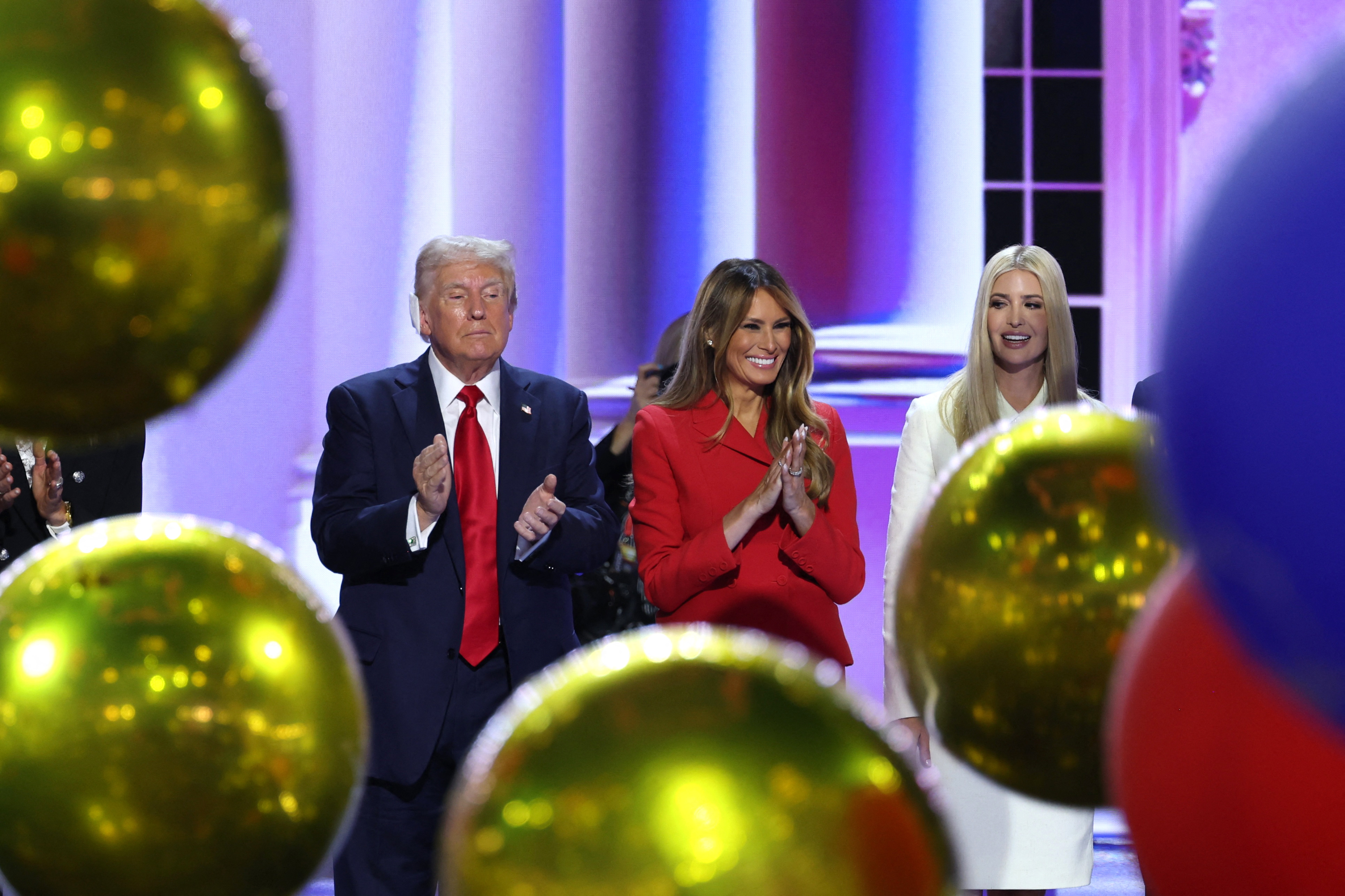 Trump and Melanie clap as gold balloons fall.