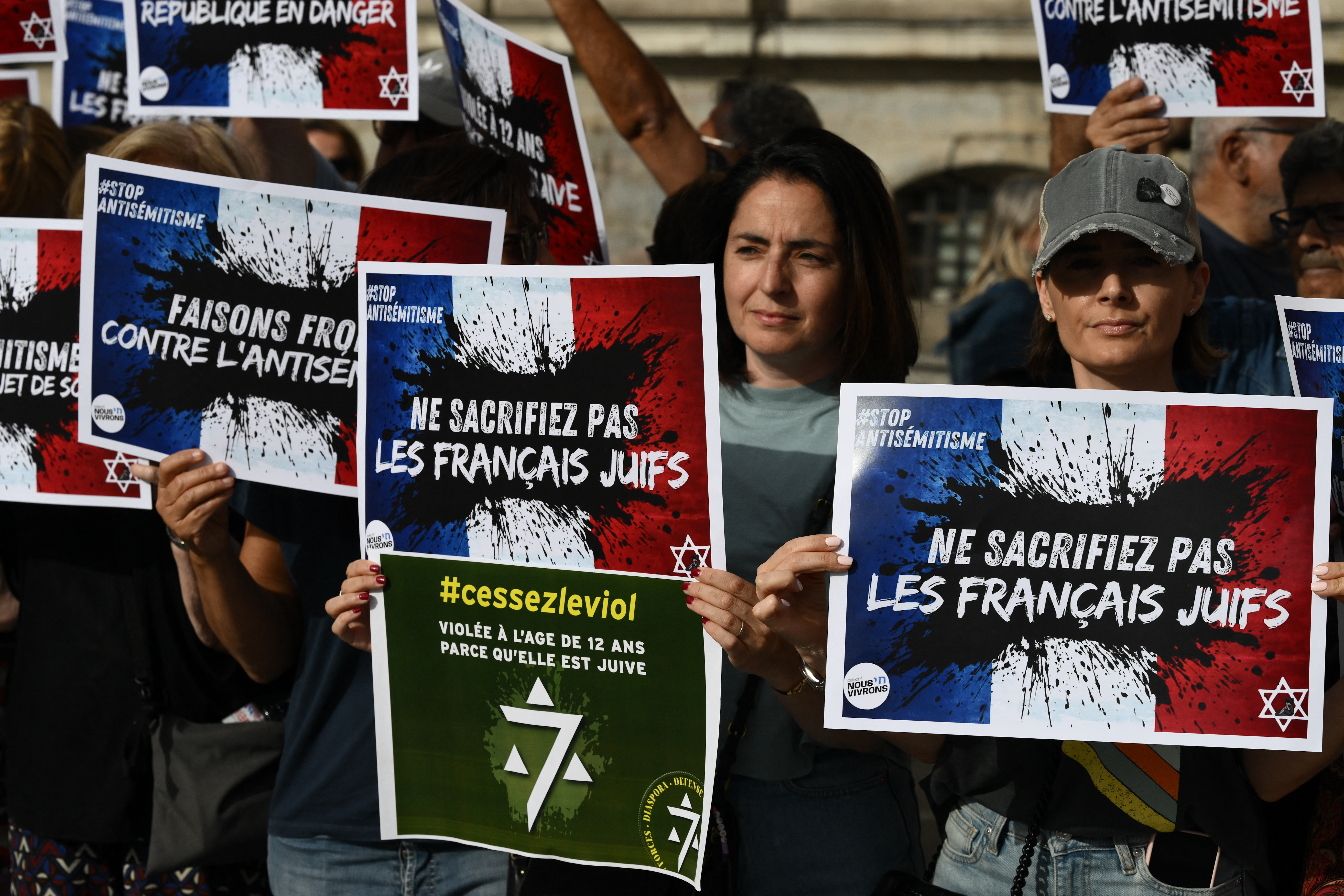 Protesters hold placards which read "Do not sacrifice French jews" as they gather to condemn the alleged anti-semetic gang rape of a 12 year-old girl, during a rally on Lyon Terreaux square in Lyon, central eastern France, on June 19, 2024. - In the midst of the general election campaign, political reactions are multiplying after the indictment on June 18, 2024, of two 13-year-olds for gang rape, death threats, anti-Semitic insults and violence against a 12-year-old girl in Paris' suburb of Courbevoie. (Photo by JEAN-PHILIPPE KSIAZEK / AFP)