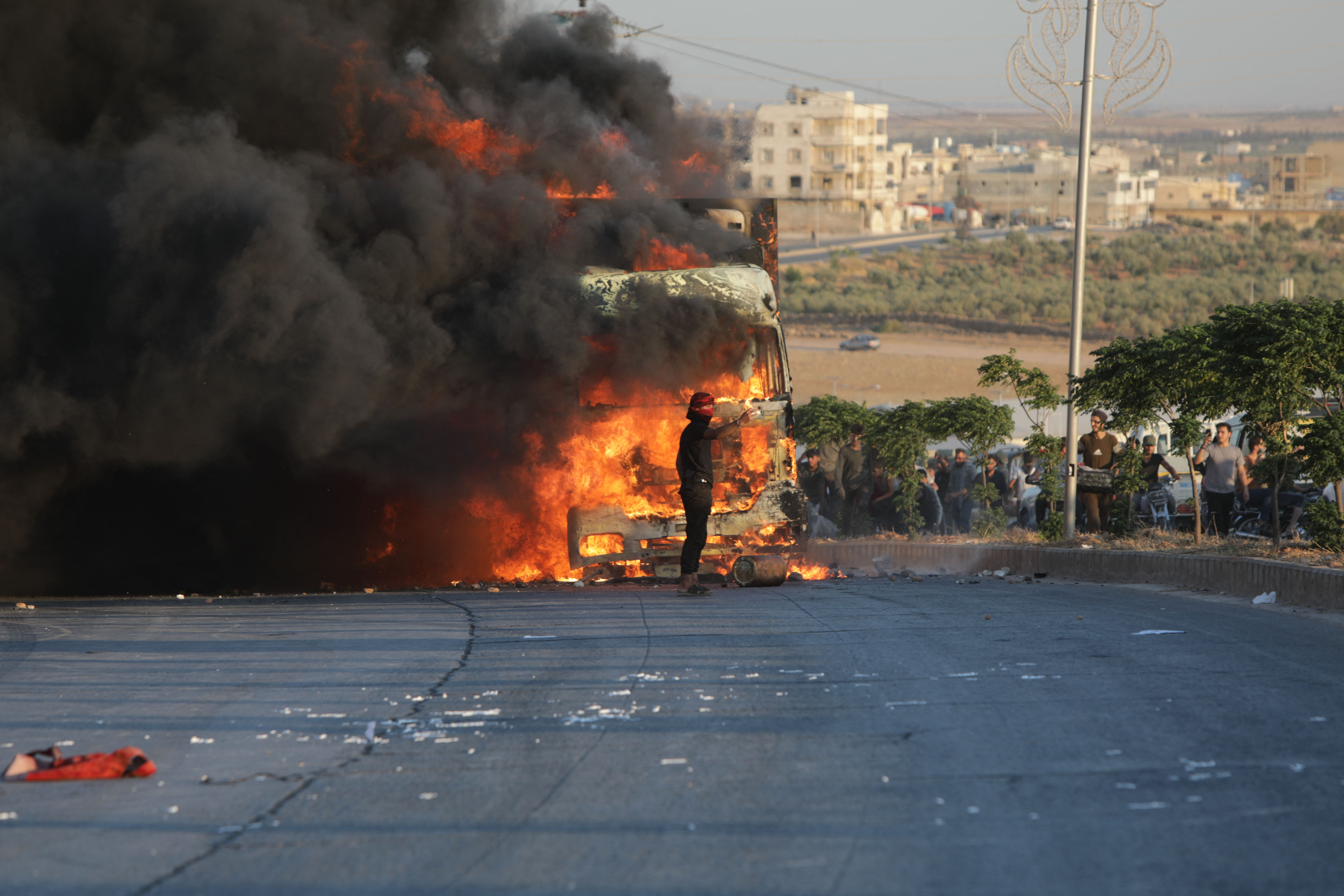A protester stands in front a burning Turkish truck during protests against Turkey in al-Bab, in the northern Syrian opposition held region of Aleppo