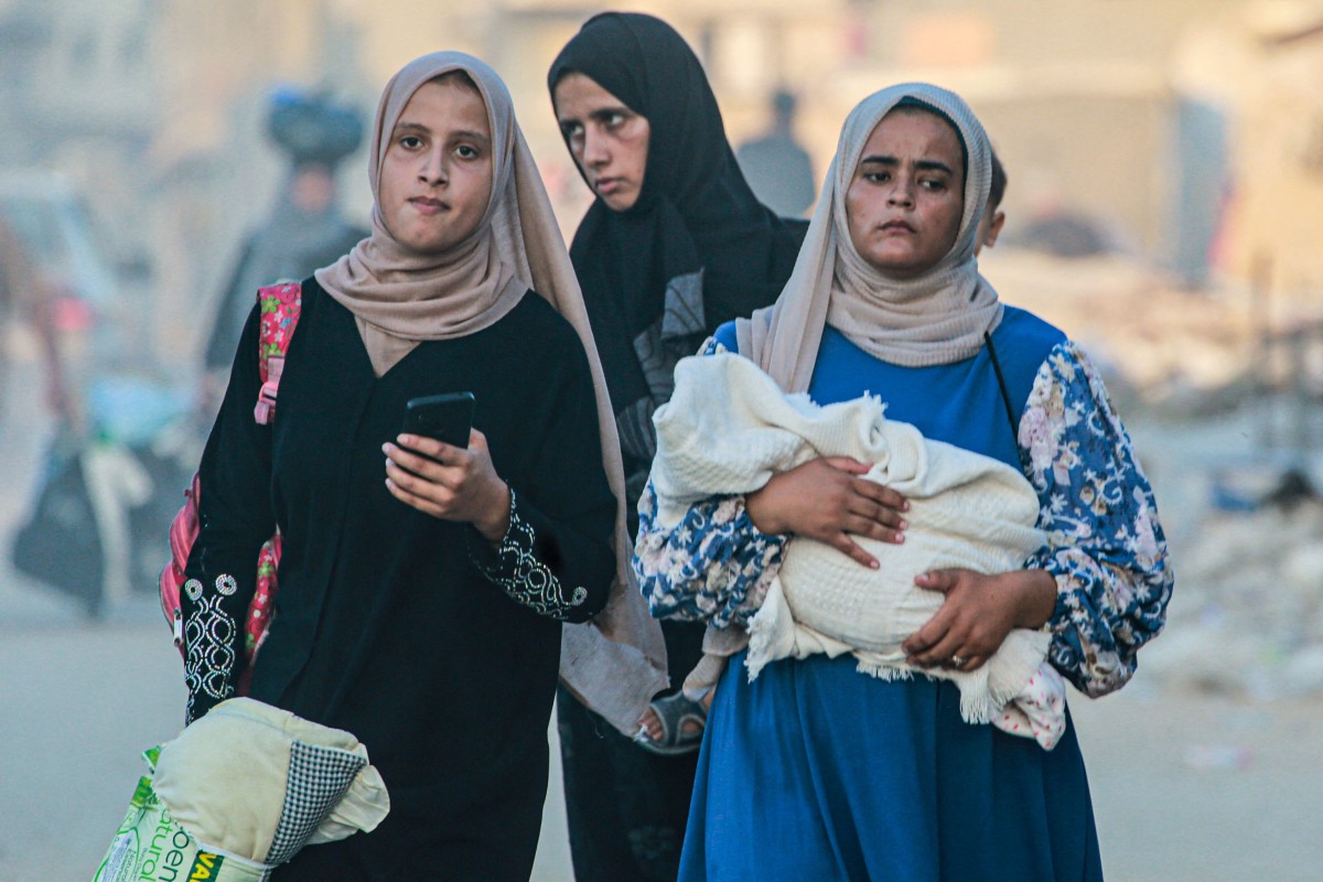A woman holds a baby wrapped in a blanket as displaced Palestinians leave an area in east Khan Yunis