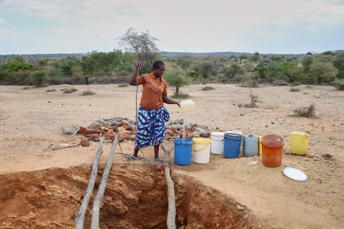 A woman pours a trickle of water into a bucket after drawing water at a village well