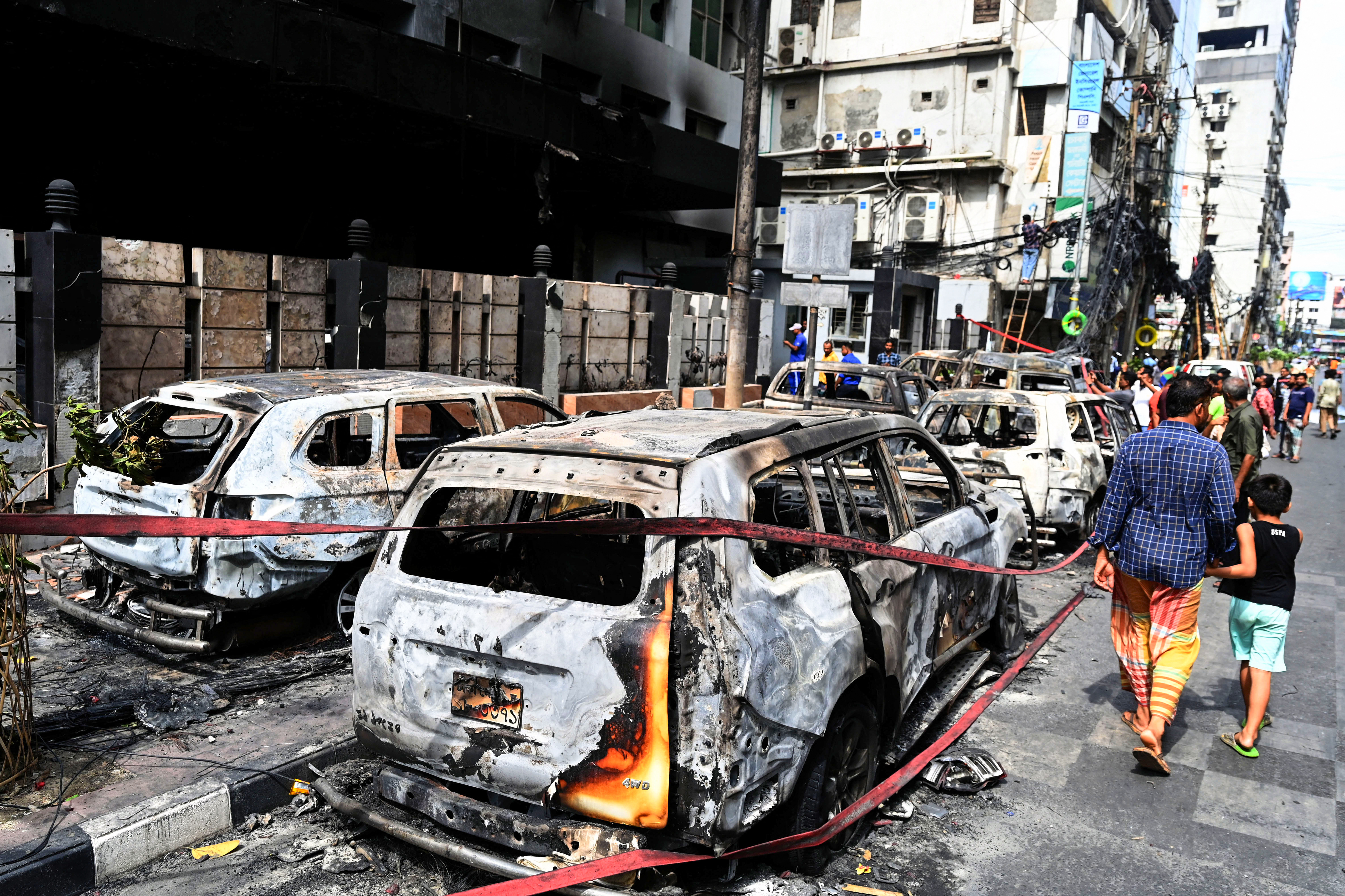 People walk past burnt vehicles after students set them on fire amid the ongoing anti-quota protest in Dhaka