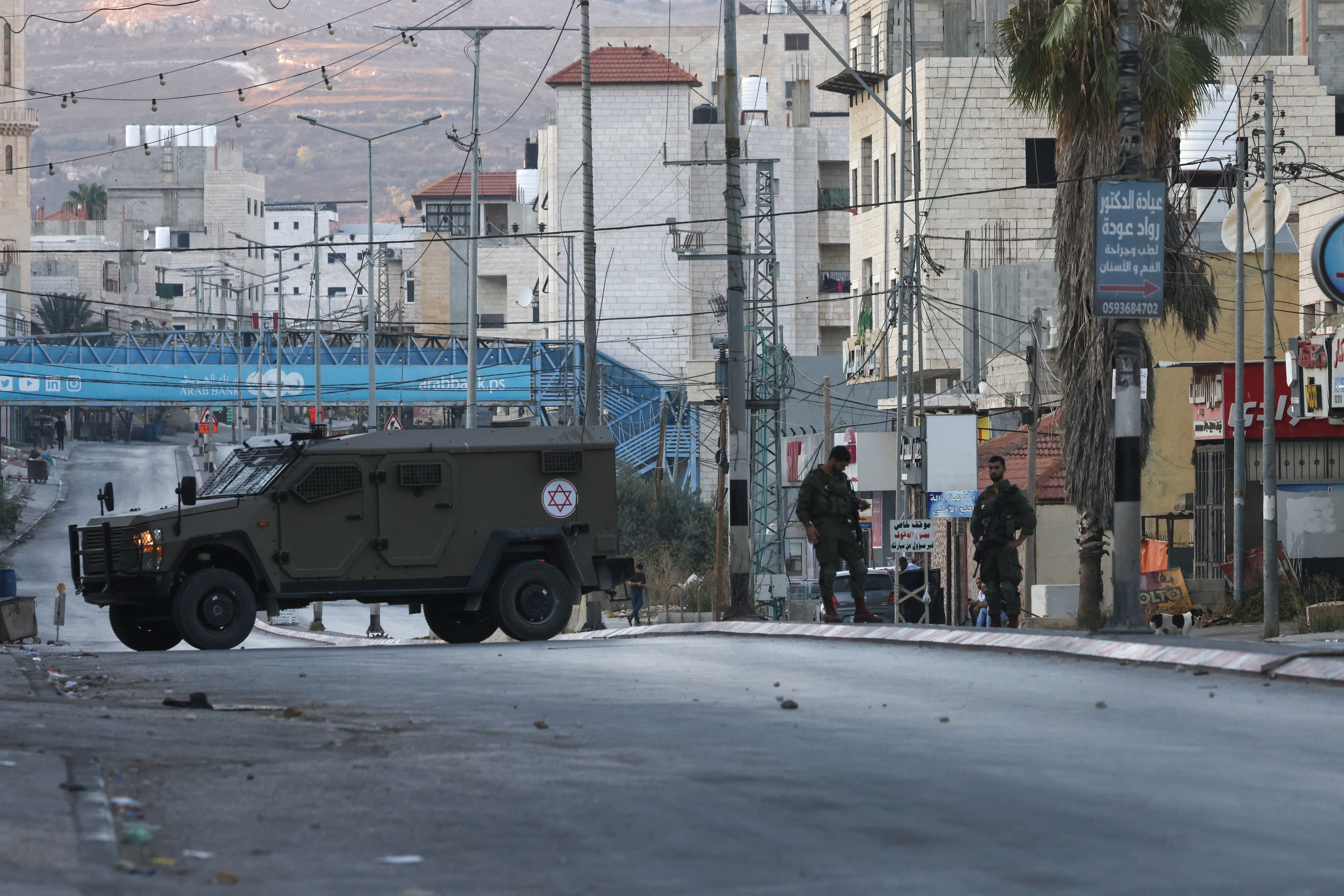 soldiers stand next to an armoured vehicle with the Star of David on it in a village