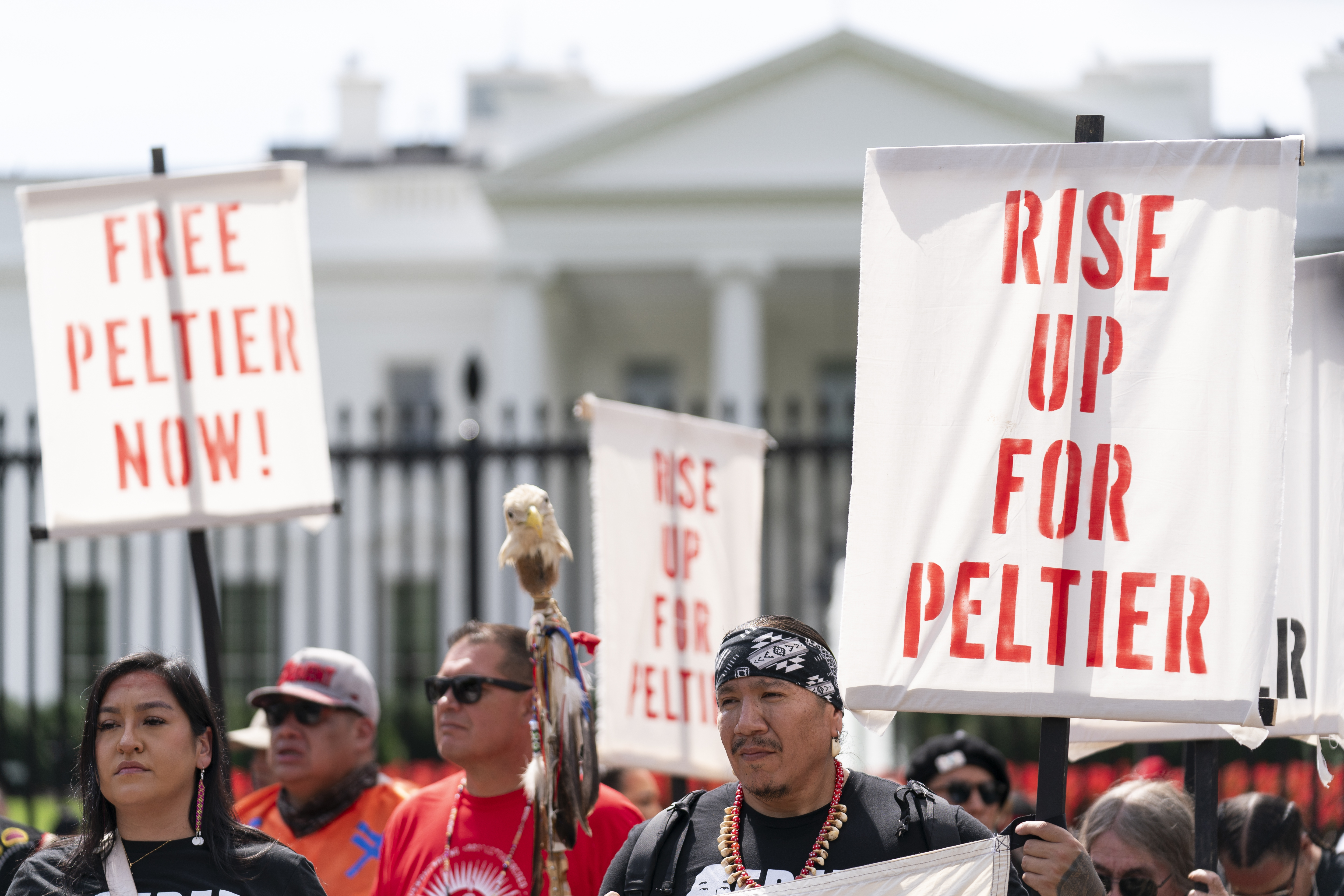 Protesters stand outside the wrought iron gate of the White House, holding up signs that read, "Rise up for Peltier."