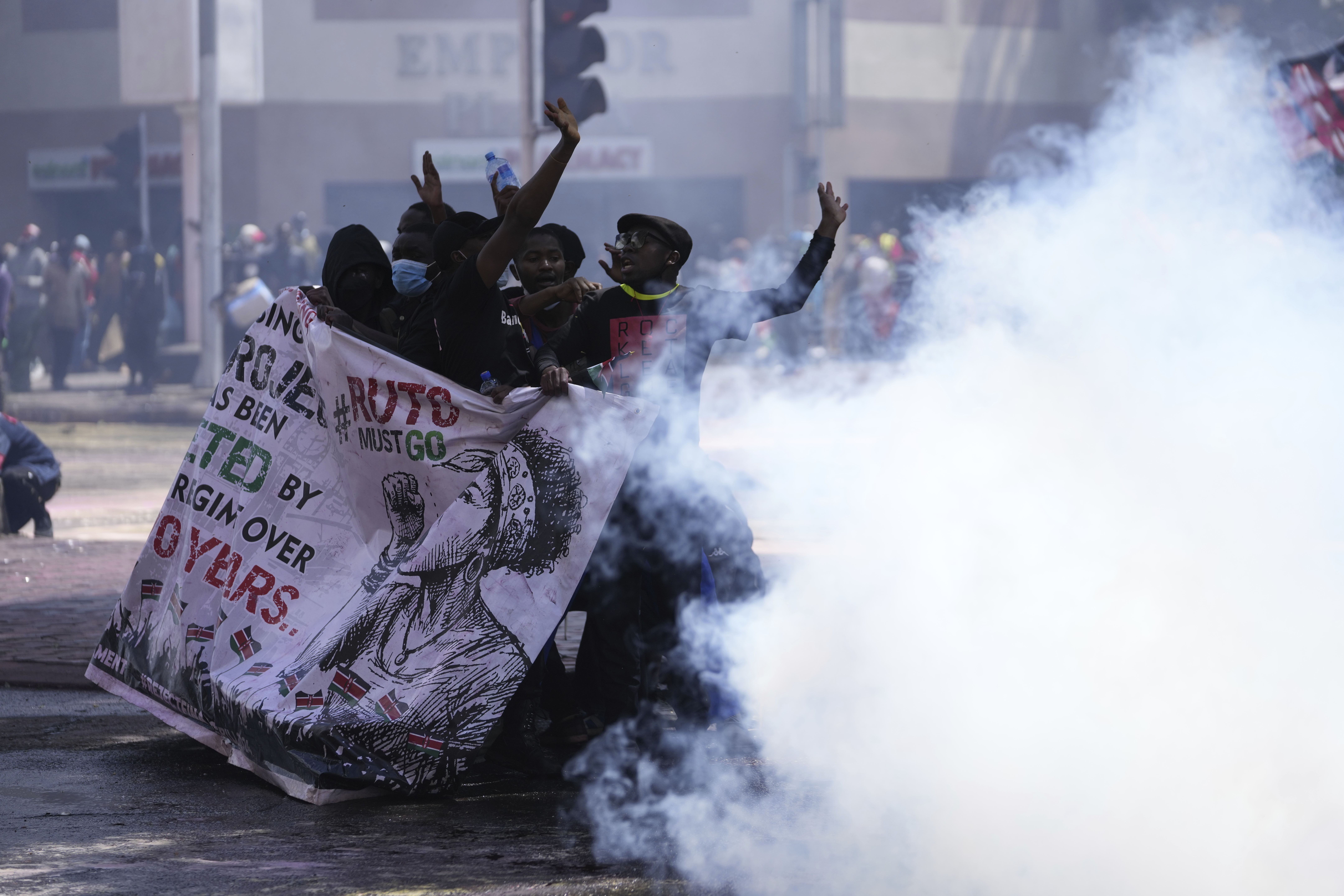 Protesters hide behind a banner as police fire tear gas at them during a protest over proposed tax hikes in a finance bill in downtown Nairobi, Kenya Tuesday, June 25, 2024. [AP Photo/Brian Inganga]