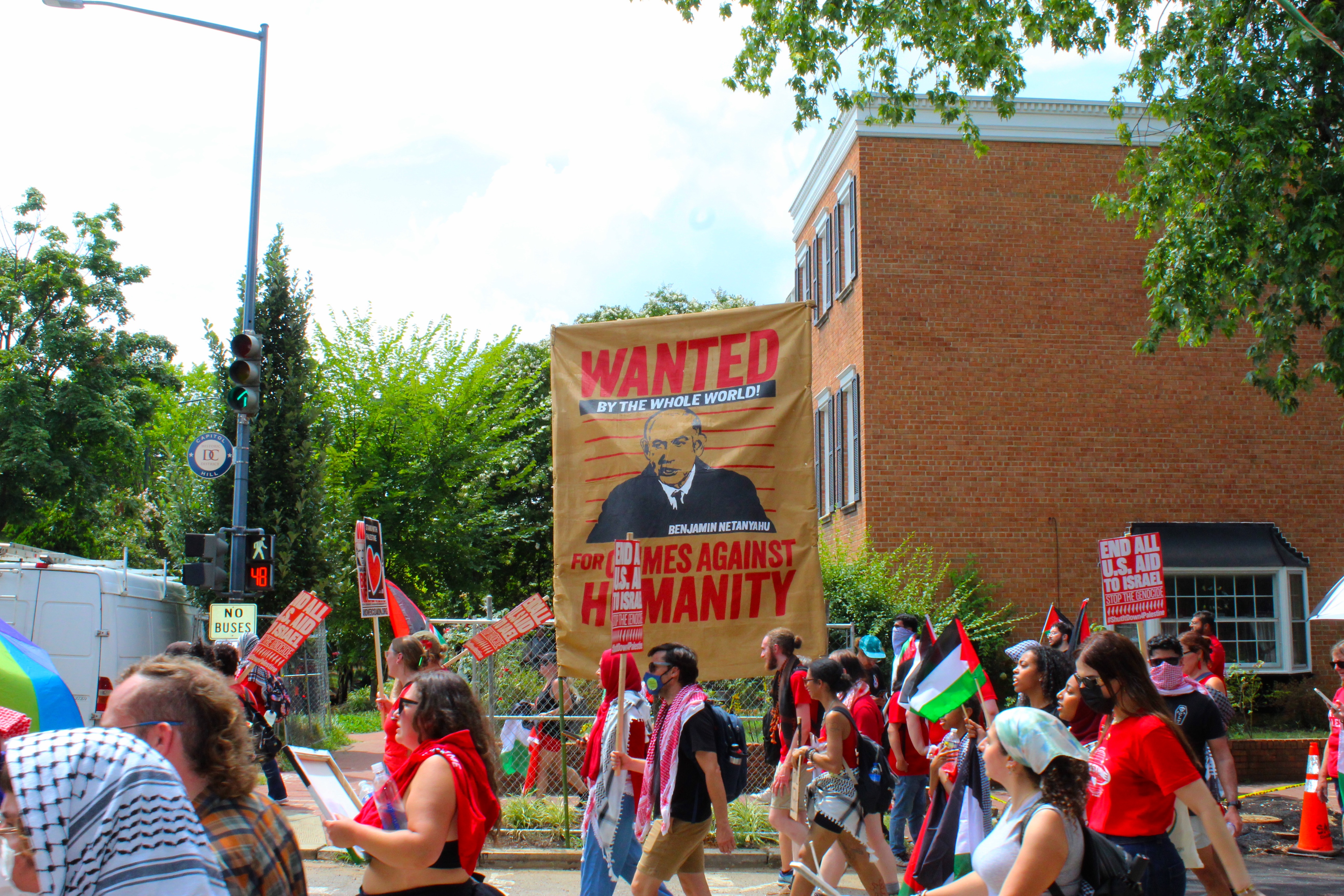 people walk past sign that reads "wanted for crimes against humanity