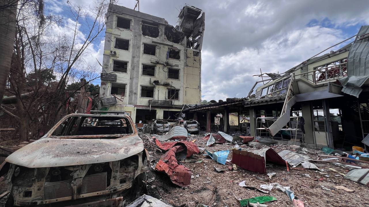 Bombed buildings and burned out cars. There is debris strewn across the ground