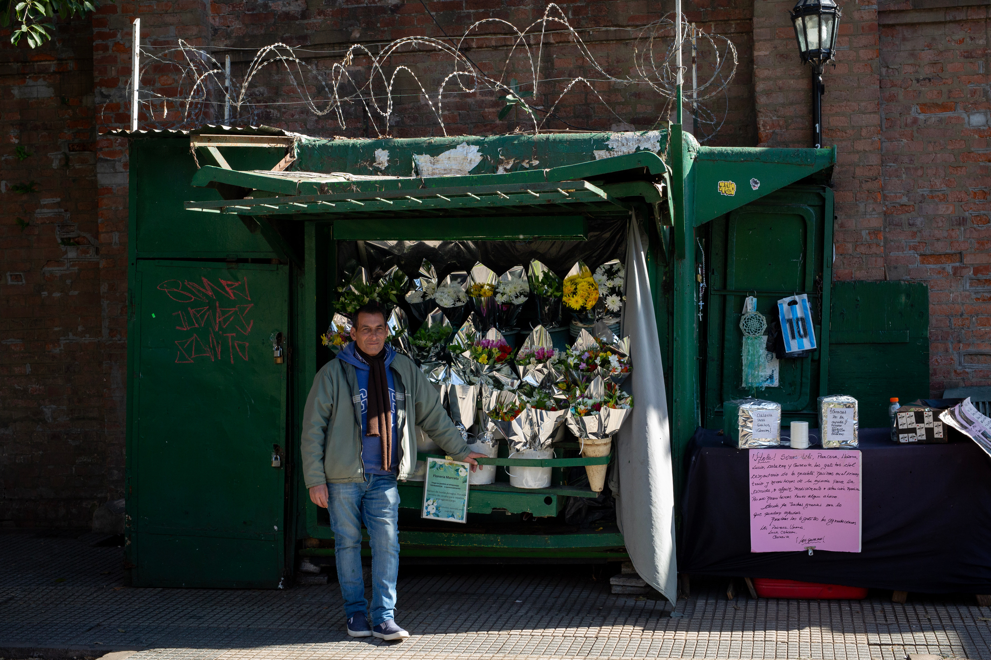 Marcelo Pisani, 55, a street florist who takes care of the feedings and well-being of the cats, poses for a photo in front of his flower stand near the entrance of the Recoleta Cemetery in Buenos Aires, Argentina on July 1, 2024. - Once home to a colony of more than 60 stray cats, the famed Recoleta Cemetery now houses only six cats: Lili, Princesa, Llorona, Lucio, Cabezn and Grisecito. Pisani, the florist, visits the cemetery every day at 5am to feed the cats. However, in a country with an ever growing economic crisis and 200% inflation, he is finding the cost of looking after the animals increasingly prohibitive and has become reliant on donations from visitors.
