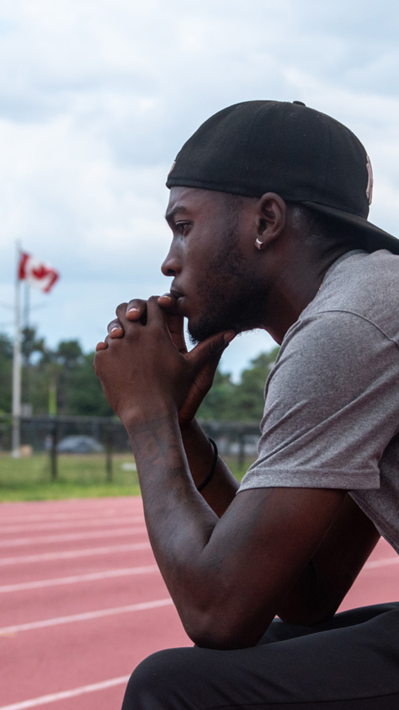 Tamarri Lindo sits on a bench, looking out over an outdoor track.
