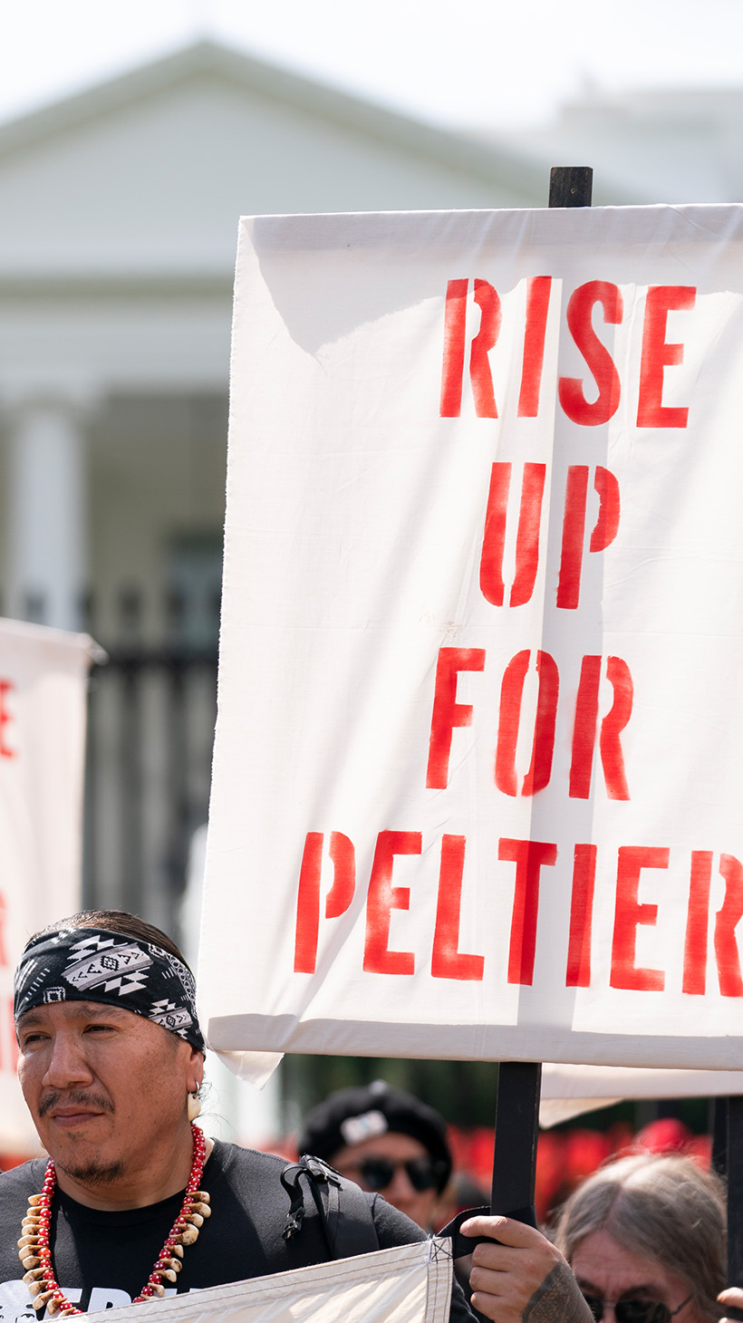 Protesters stand outside the wrought iron gate of the White House, holding up signs that read, "Rise up for Peltier."