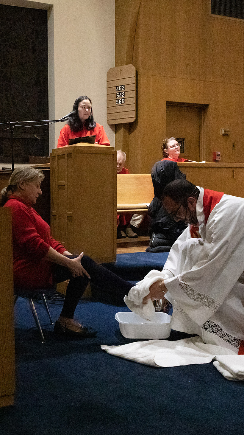 Pastor Khalilia kneels in his white robes to wash the feet of a parishioner at the front of the church.