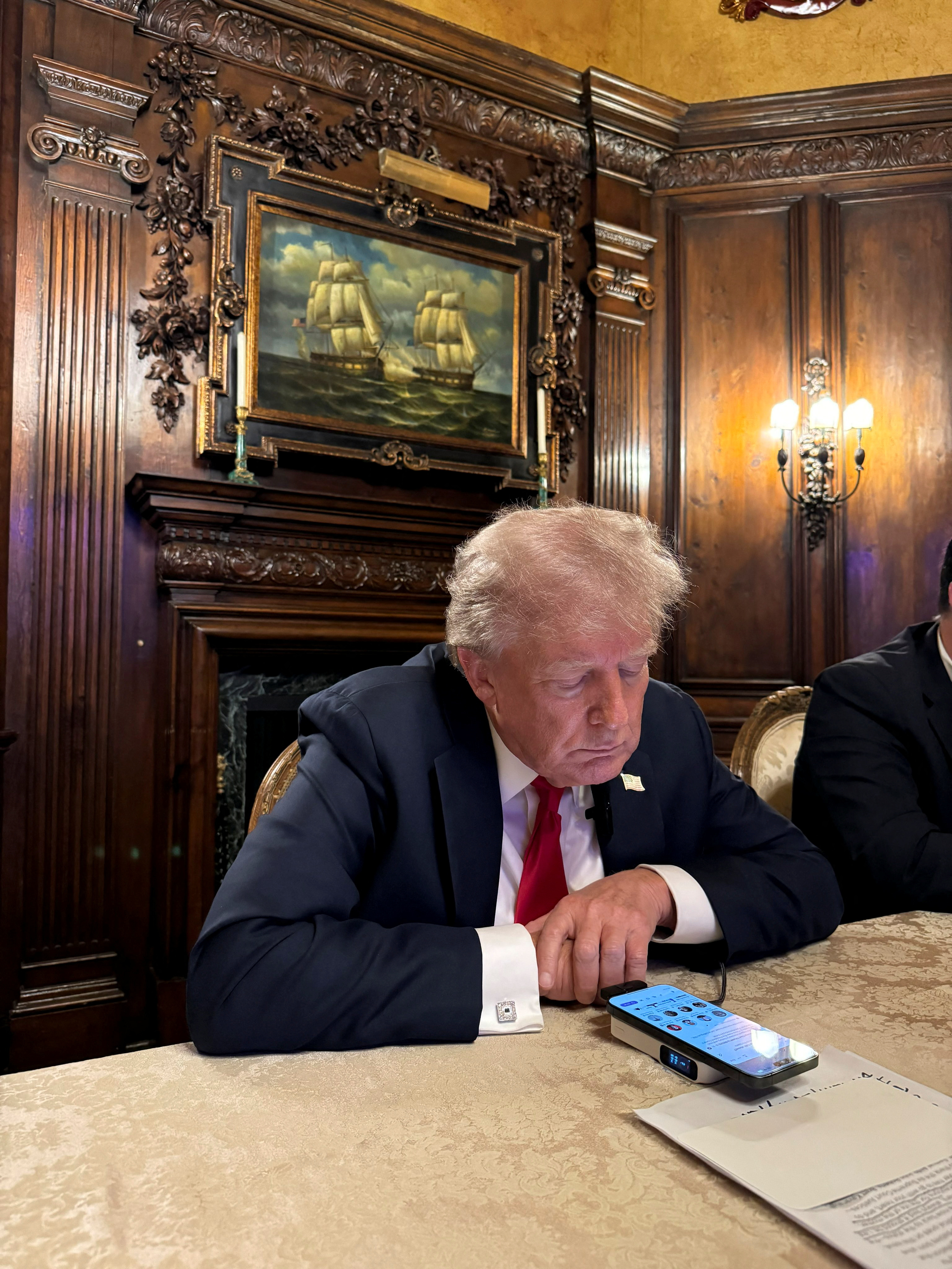 Trump during his chat with Musk. He is hunched over his phone. He is sitting in a wood-panelled room.