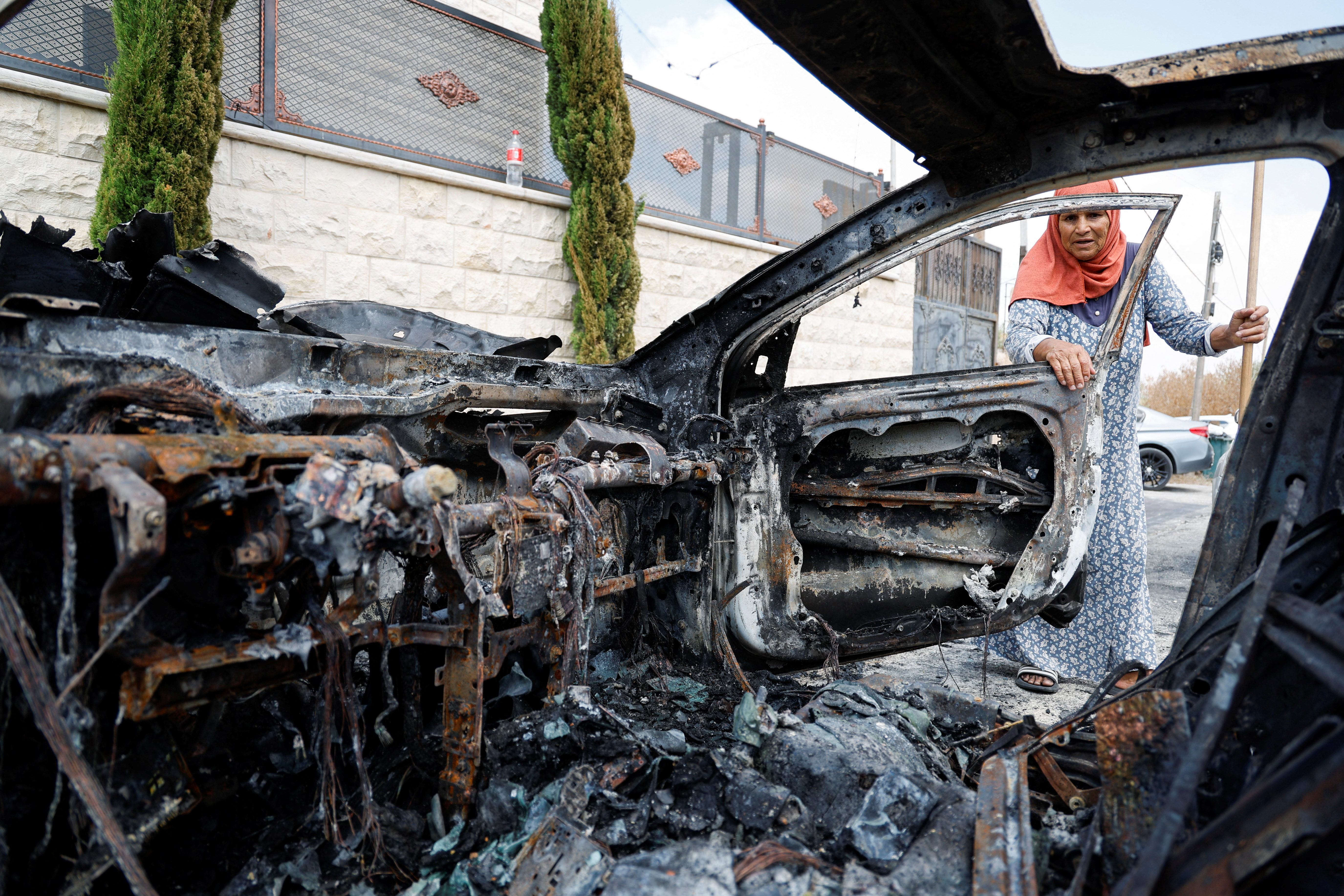 A Palestinian woman looks at a car destroyed in an Israeli settler attack in Jit, West Bank
