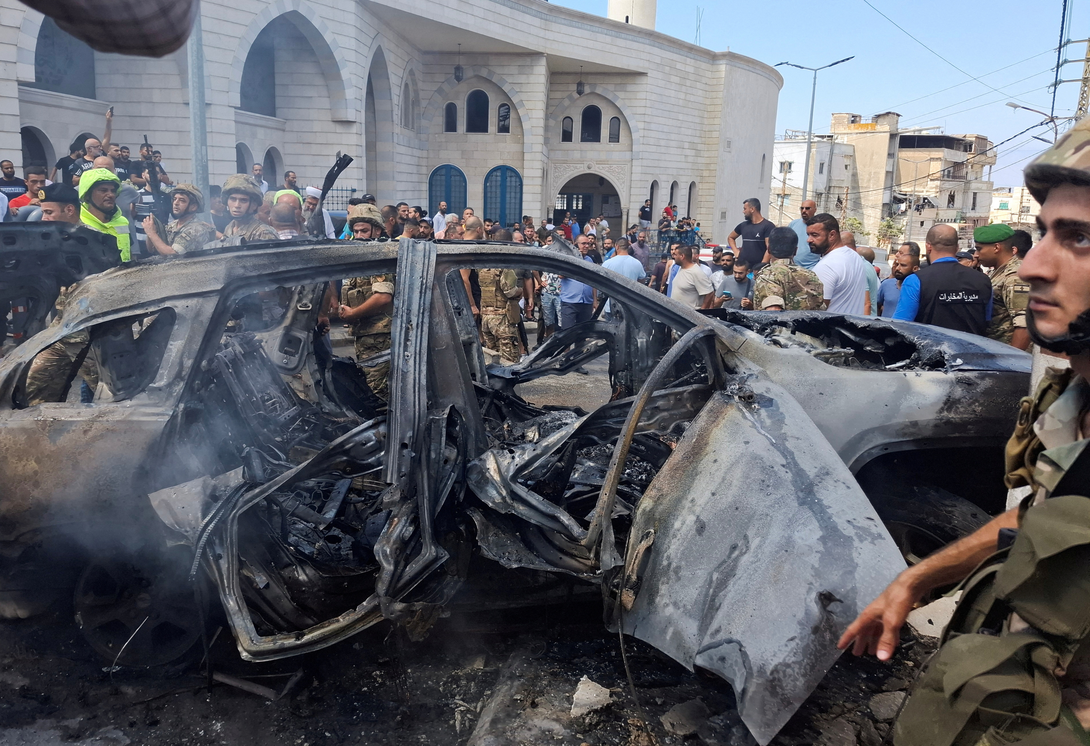 People and Lebanese army members stand near a burnt car after an Israeli strike on the outskirts of the southern port city of Sidon, according to two Palestinian sources, in Lebanon August 21, 2024. REUTERS/Hassan Hankir TPX IMAGES OF THE DAY