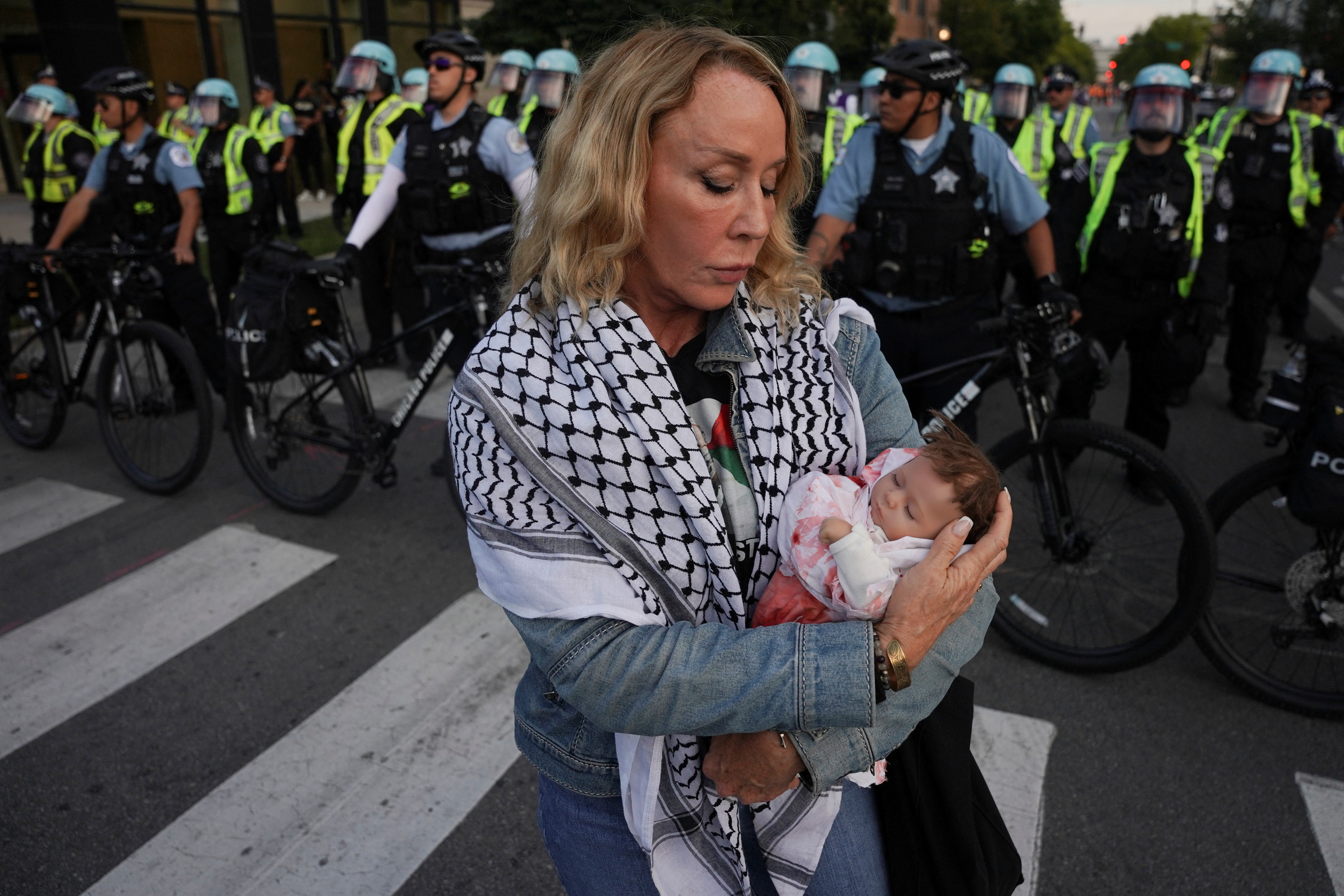 A protester in a keffiyeh cradles a baby doll in front of a line of police