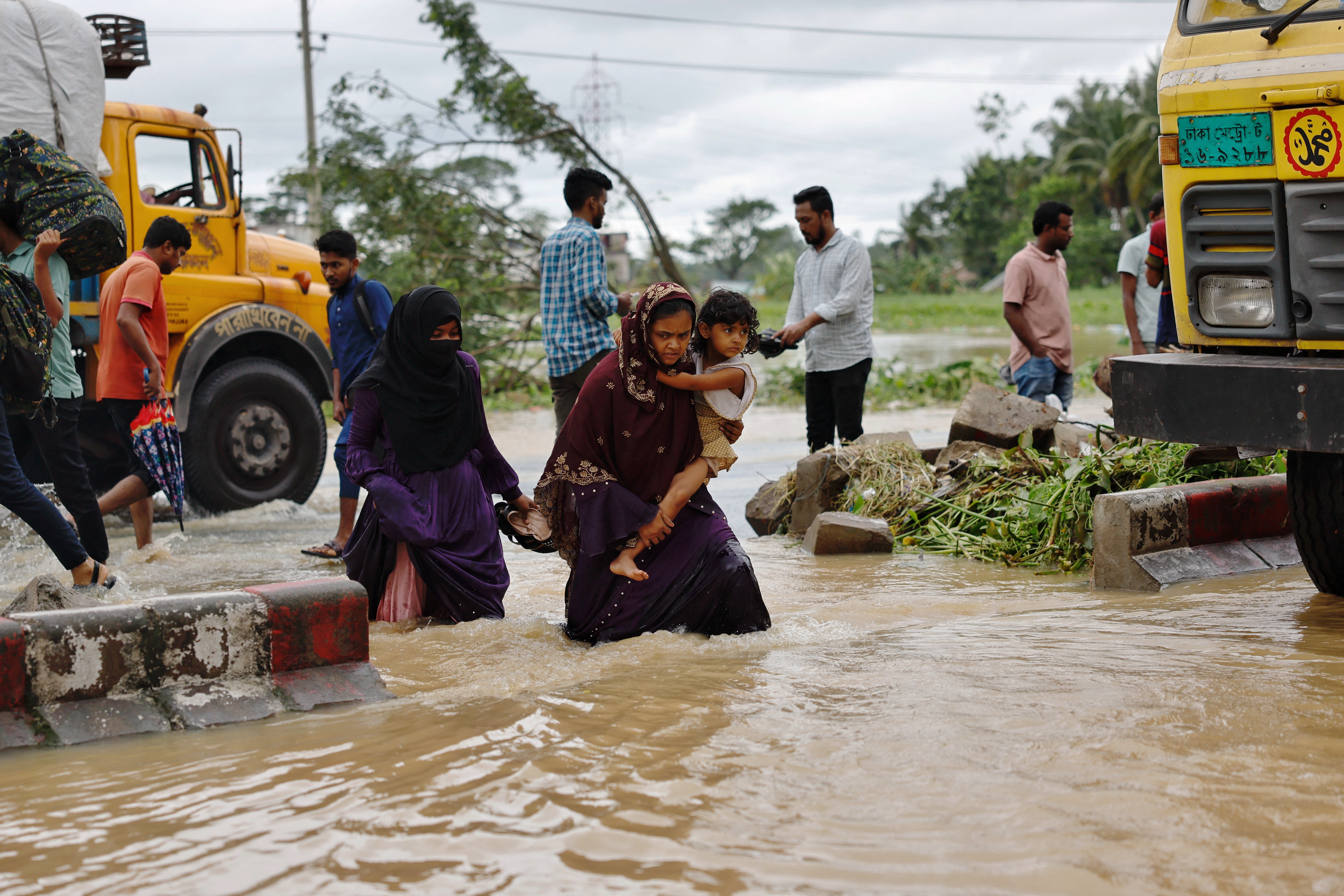 Women with a child cross a flooded street after a severe flood in the Lalpol area in Feni,