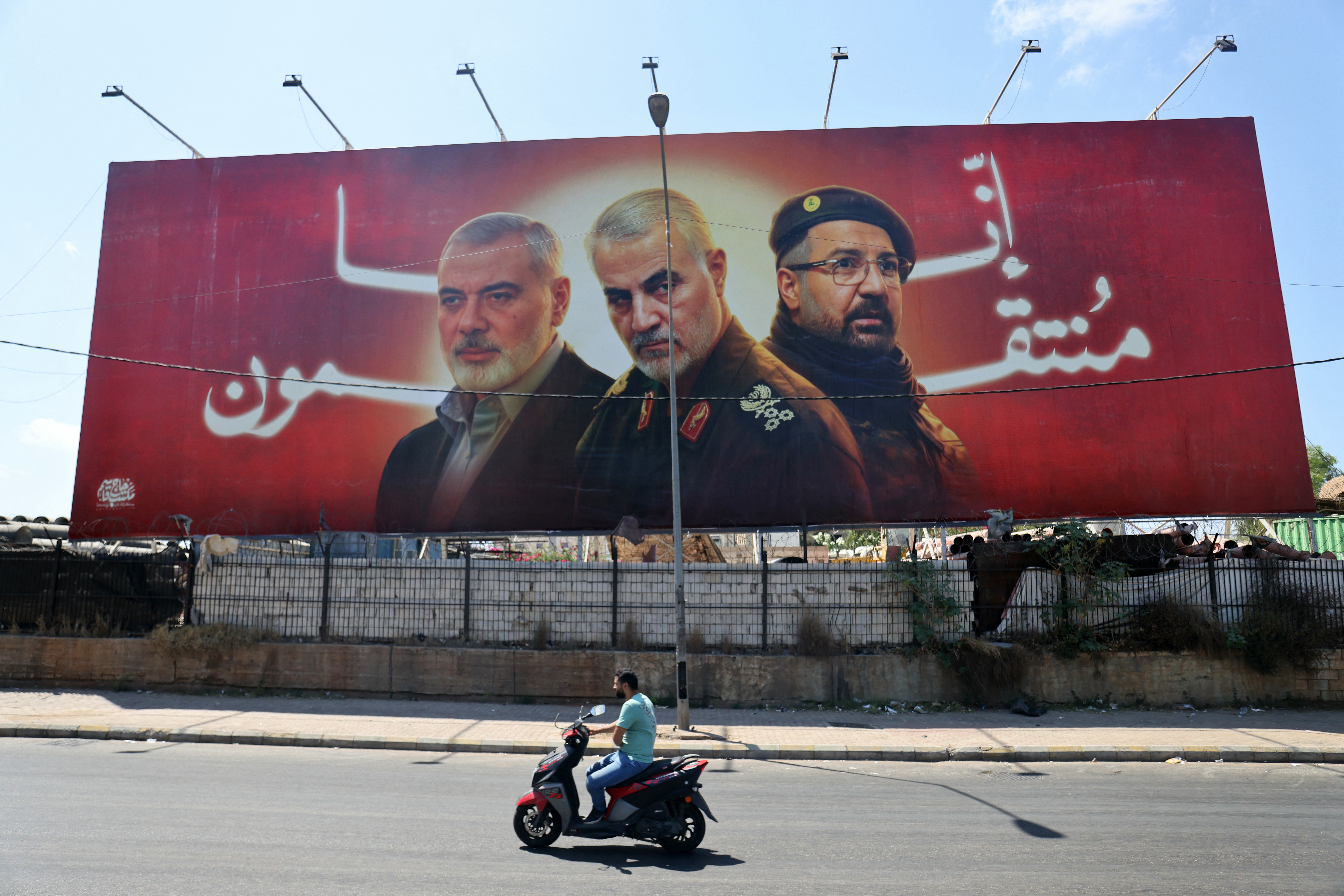 TOPSHOT - A man rides his moped past a billboard bearing portraits of slain leaders, Ismail Haniyeh of the Palestinian militant group Hamas, Iranian Quds Force chief Qasem Soleimani (C), and Hezbollah senior commander Fuad Shukr on the main road near the Beirut International Airport on August 3, 2024. (Photo by Ibrahim AMRO / AFP)