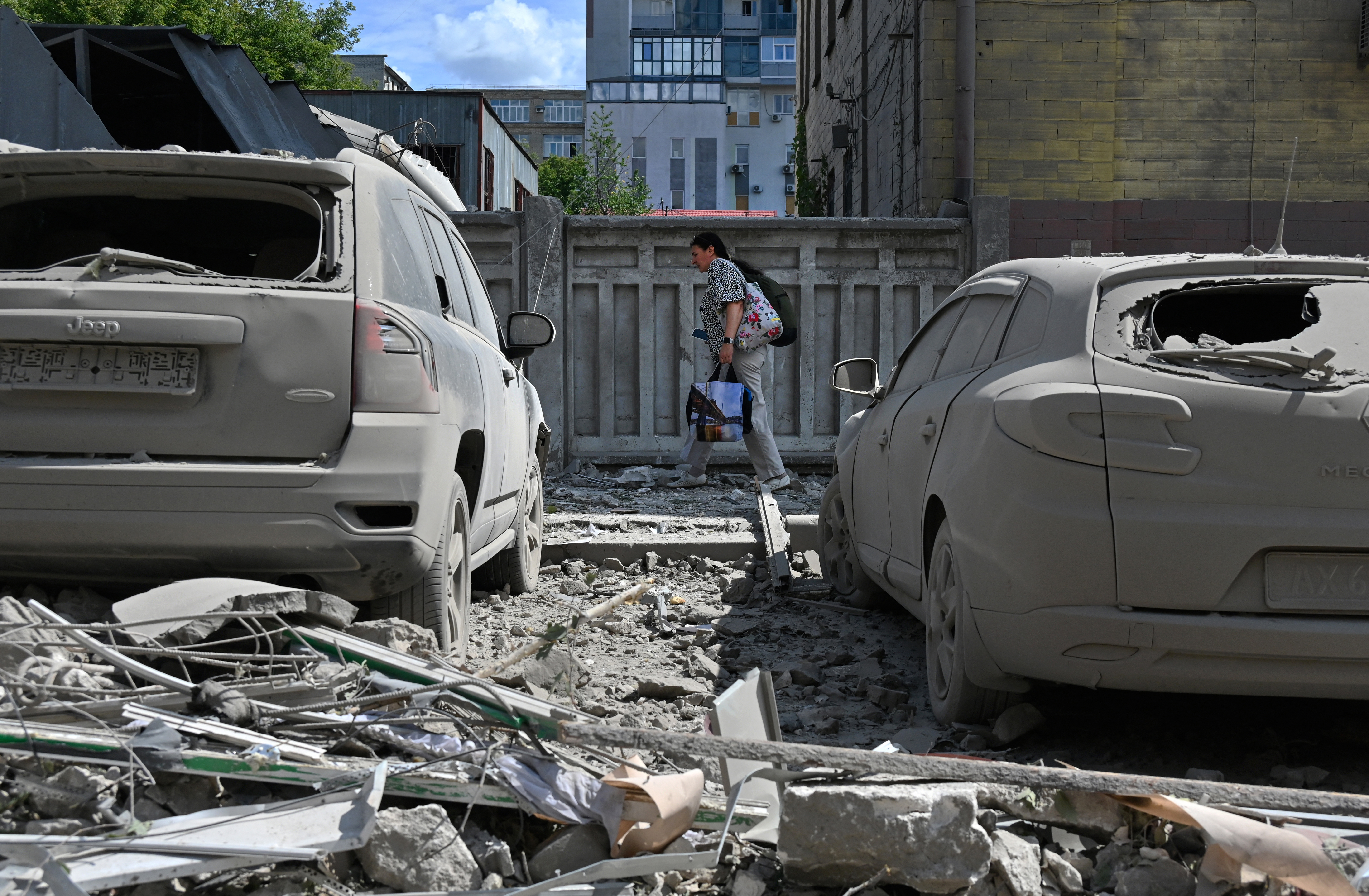Cars covered in debris and dust after a Russian missile attack on Kharkiv. A man is walking behind.