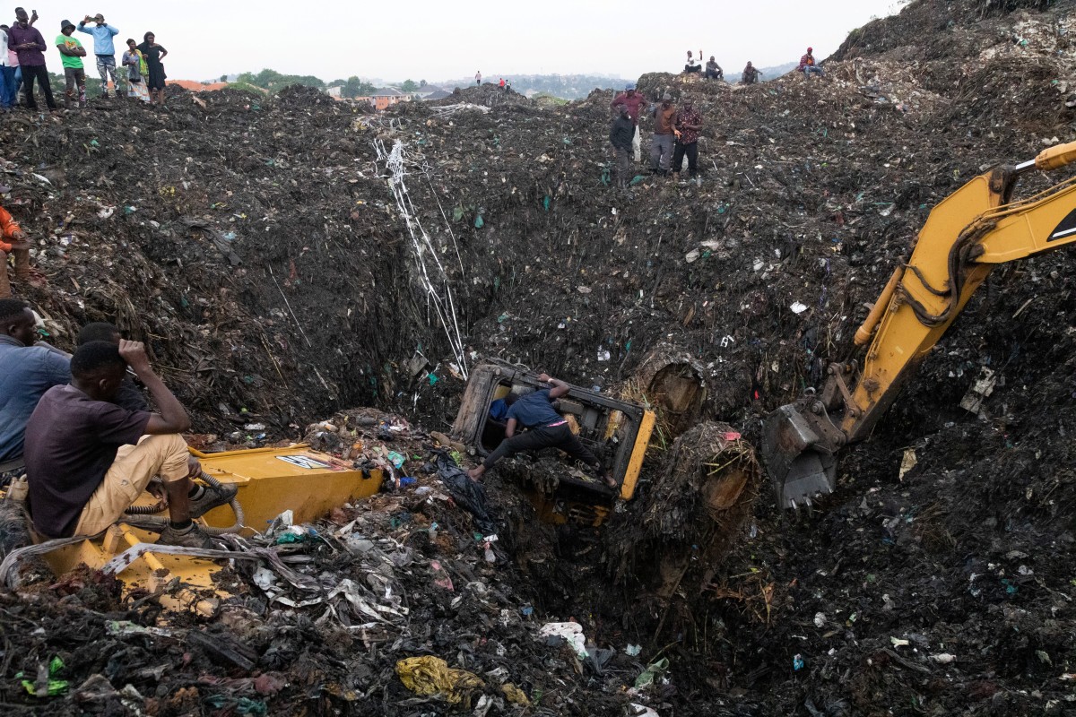 People search inside a damaged excavator while searching for a driver trapped under debris after a landfill collapsed in Kampala on August 10, 2024. - Eight people including two children were killed when mountains of garbage collapsed at a landfill in the Ugandan capital Kampala on August 10, the city authority said. (Photo by BADRU KATUMBA / AFP)