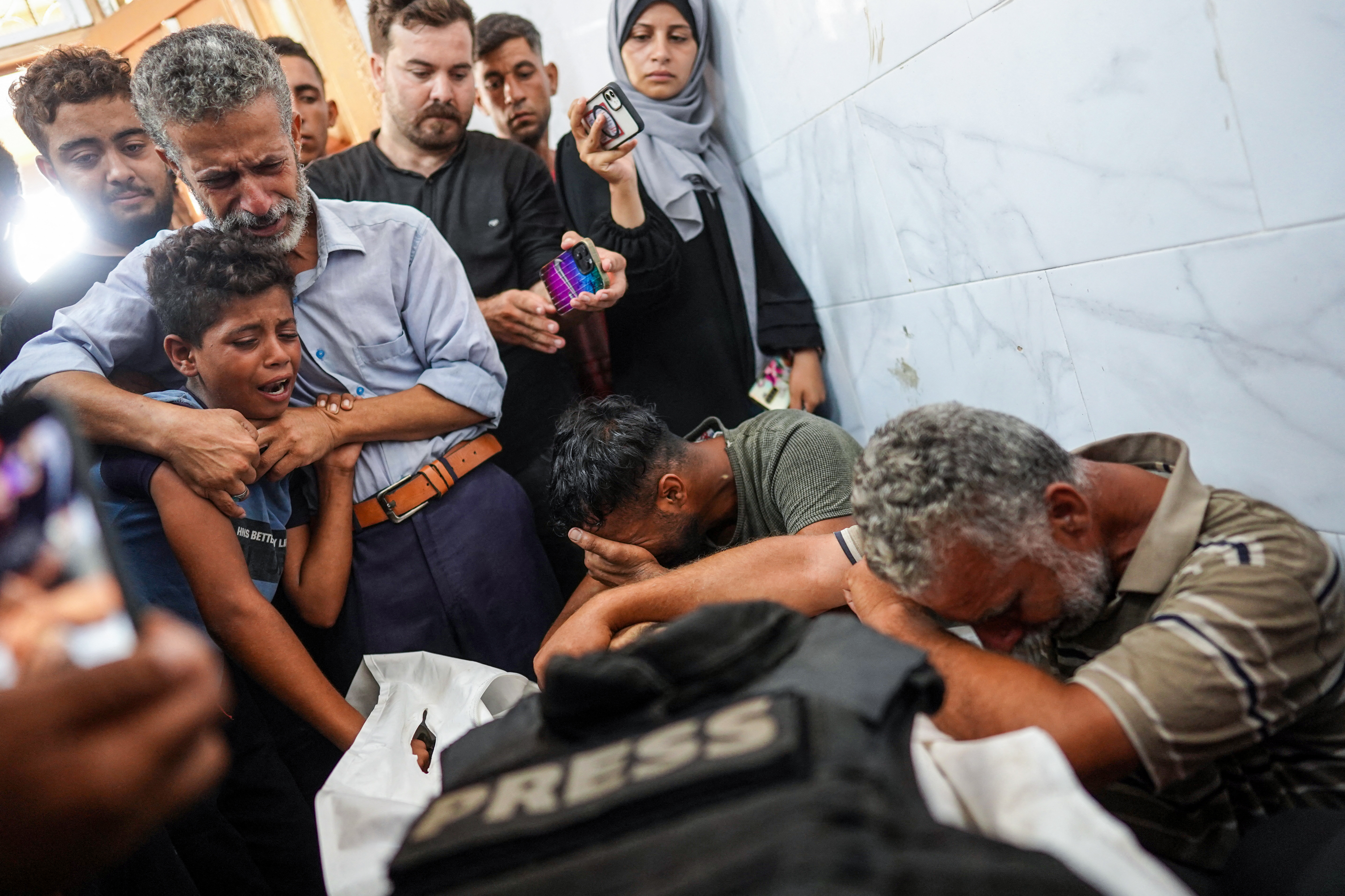 people gather around mourning a body covered in a press vest