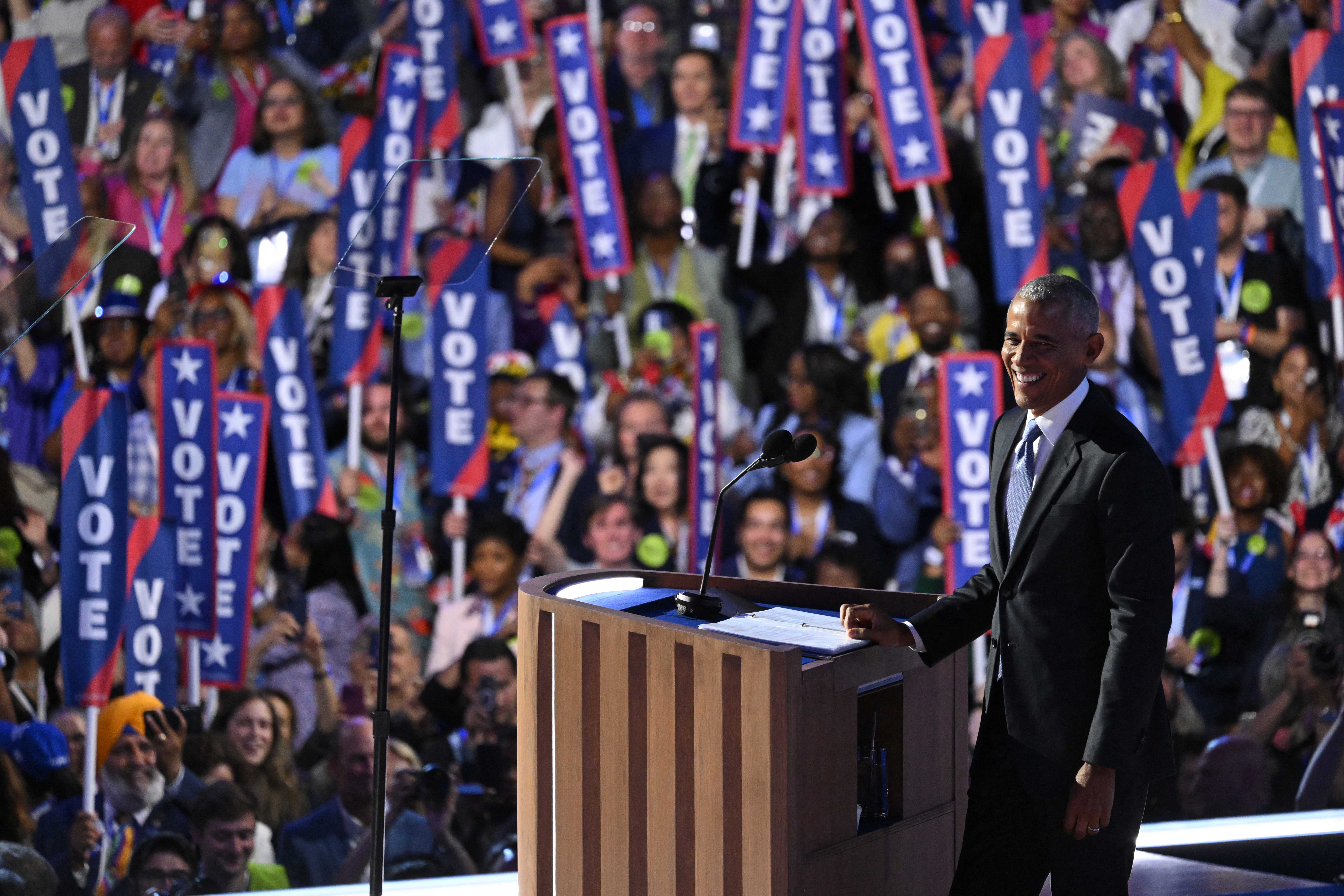 Barack Obama on stage. The crowd is behind. They are holding banners reading 'VOTE'. Obama is smiling.