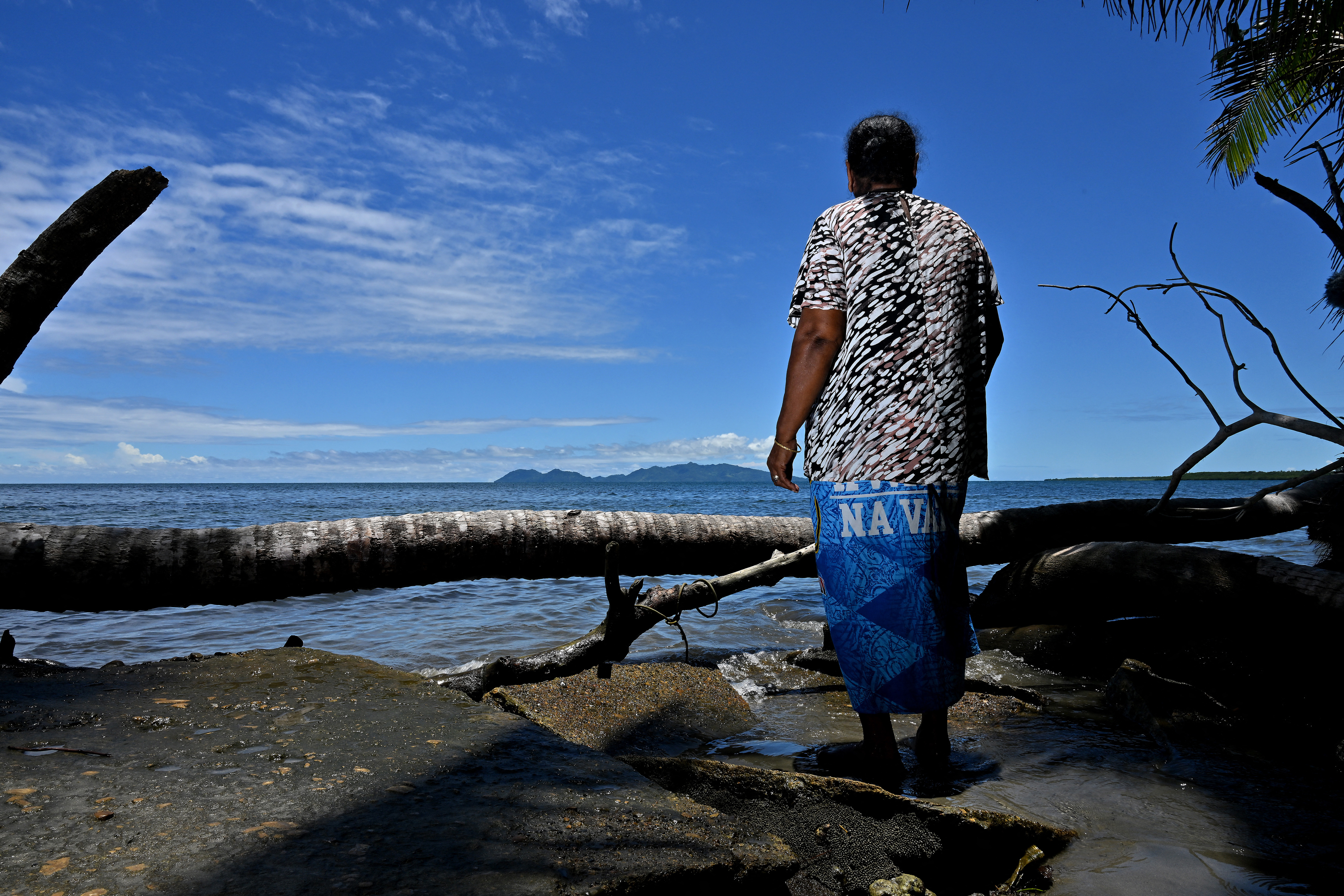 A woman looks out to the sea in Fiji, The beach has been eroded.