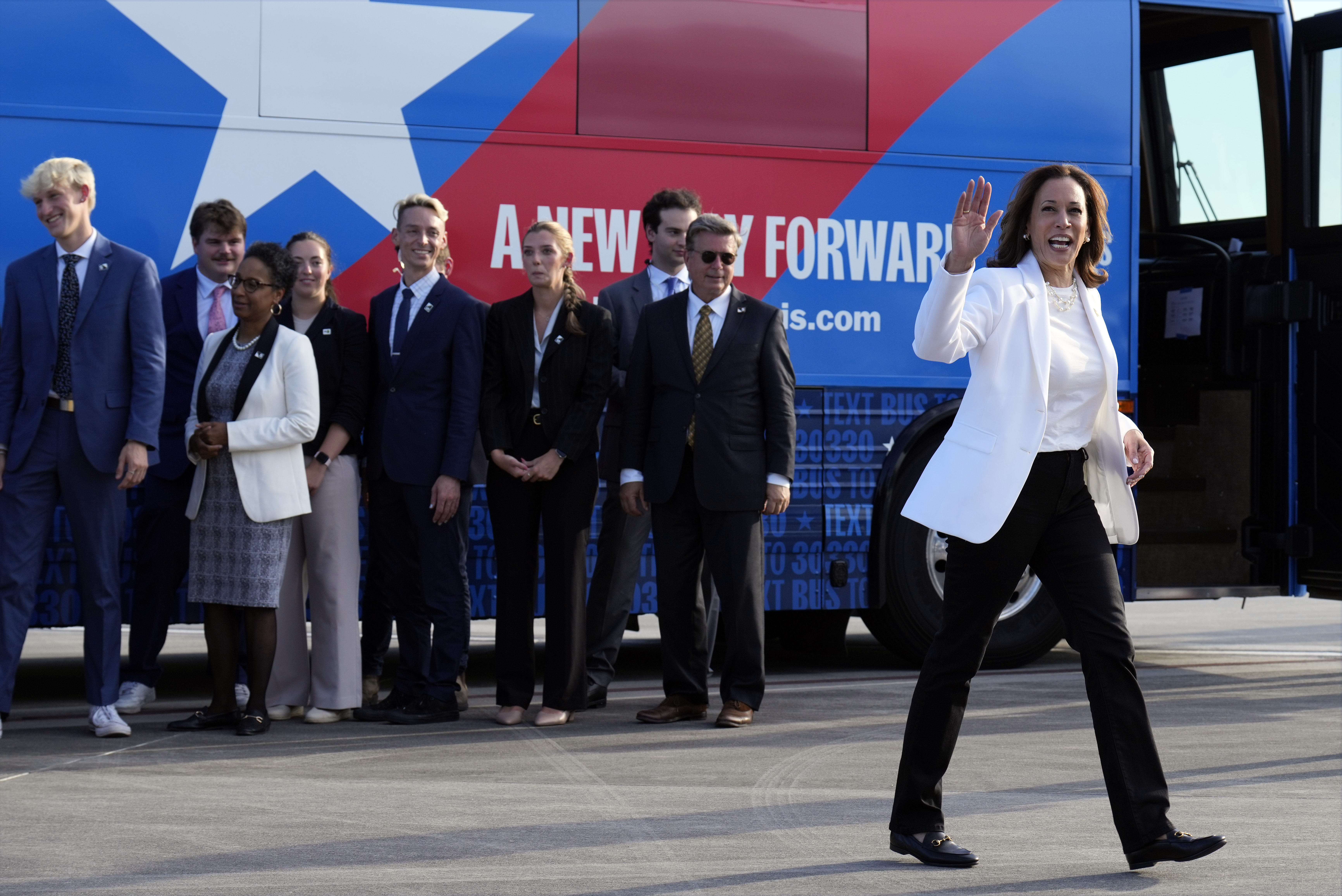Kamala Harris disembarks a branded campaign bus, surrounded by staffers and supporters.