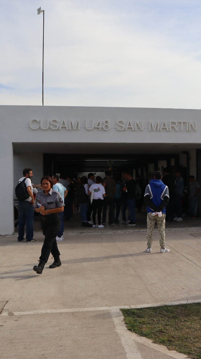 People stream in and out of a low-slung concrete building, labelled, "CUSAM U48 San Martin"
