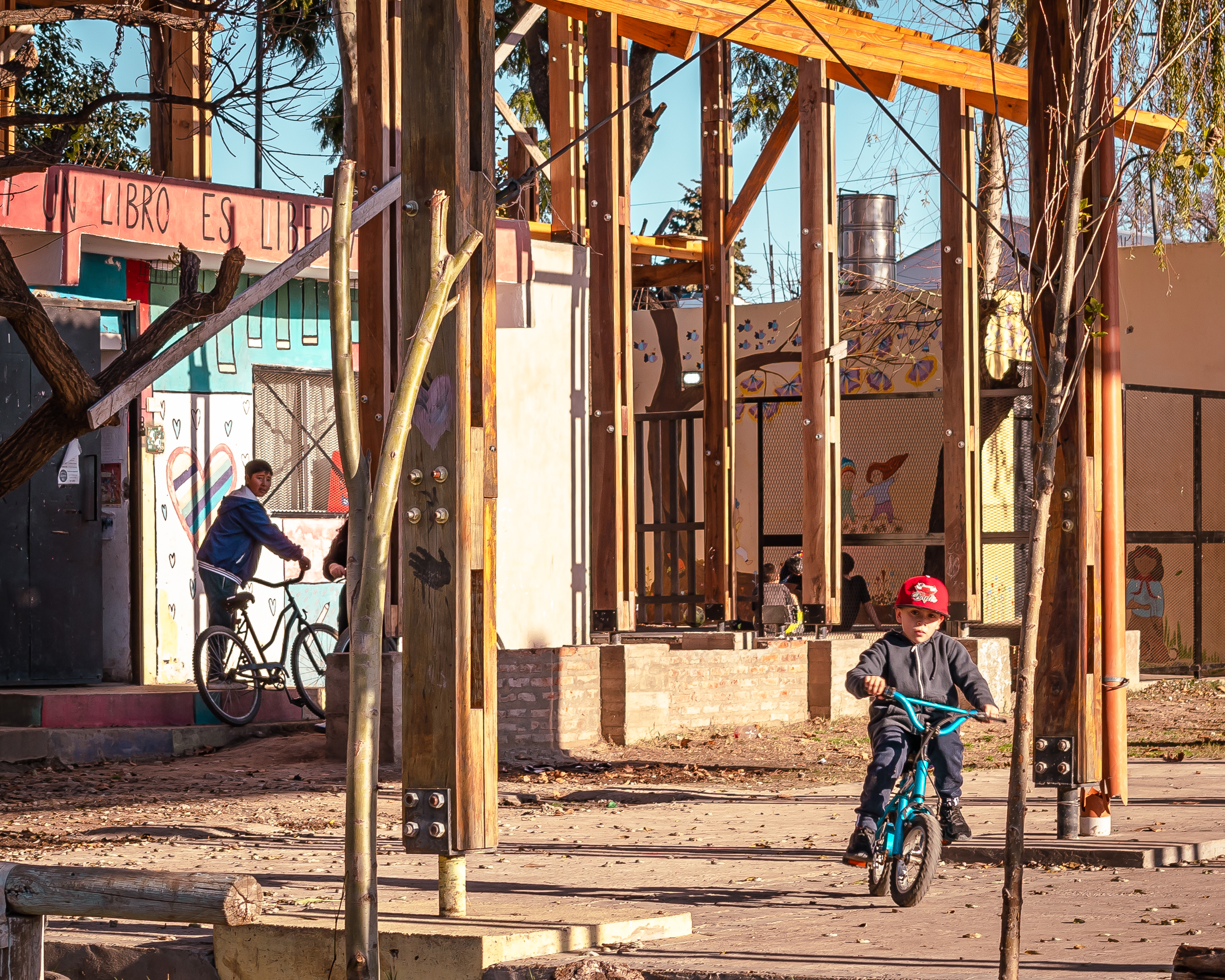 Kids ride bicycles beneath the scaffolding of the future La Corcova library