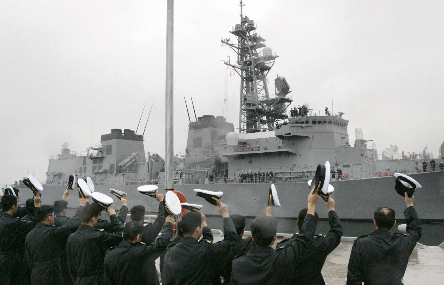 The Sazanami sailing out of port. Sailors are lined up on the quay waving their hats