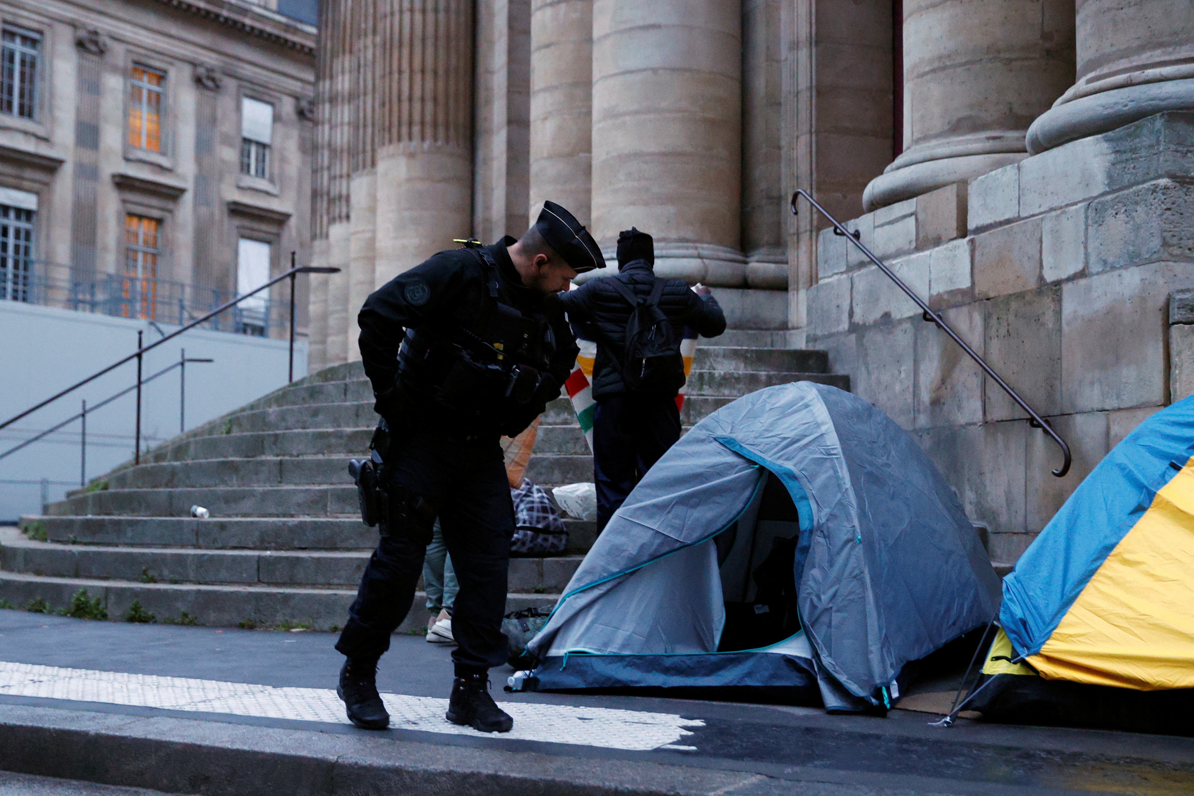 A French Gendarme looks at a migrant tent