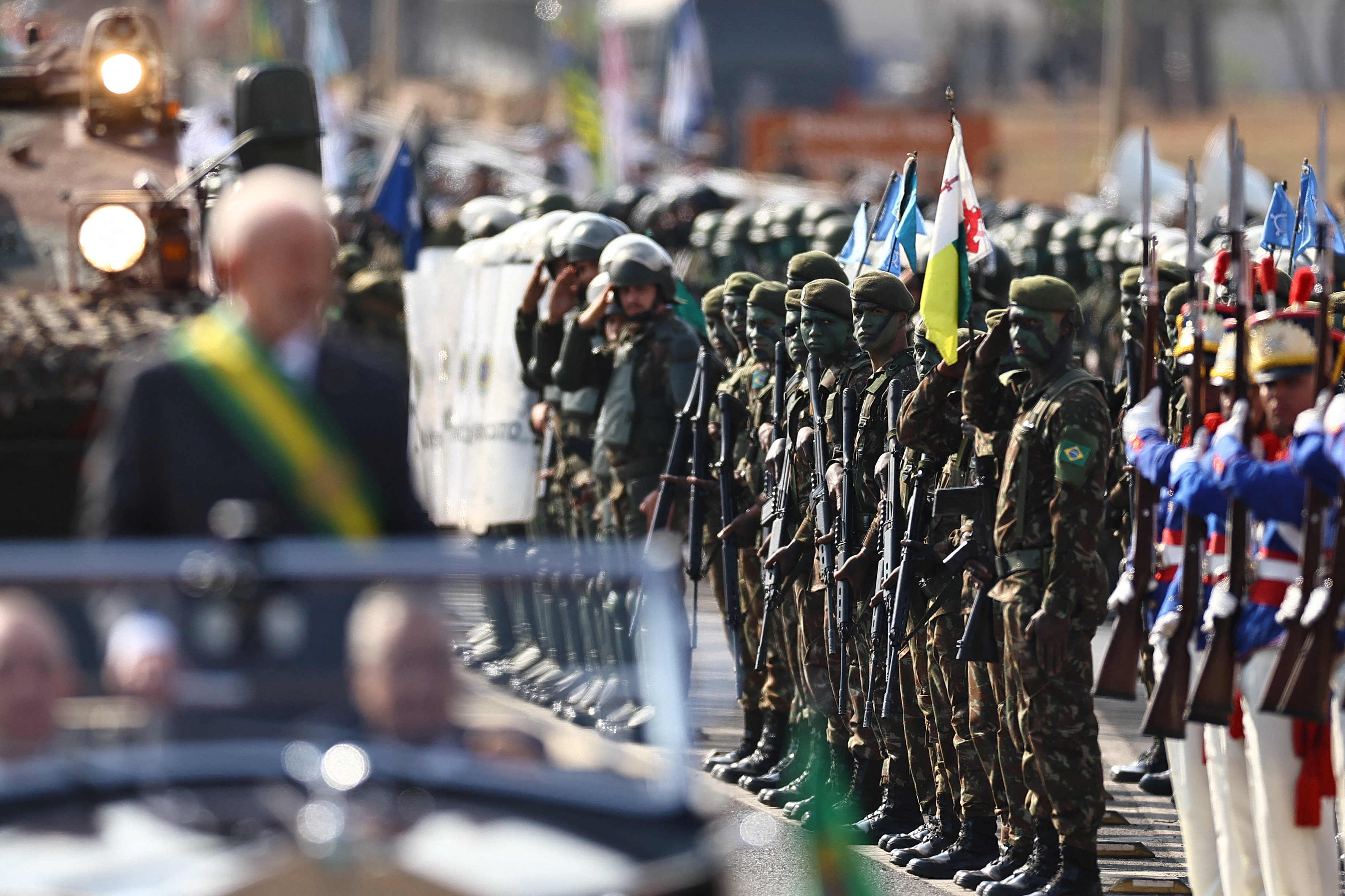 President Lula da Silva stands in the back of a convertible vehicle during a parade, passing military members lined up at attention