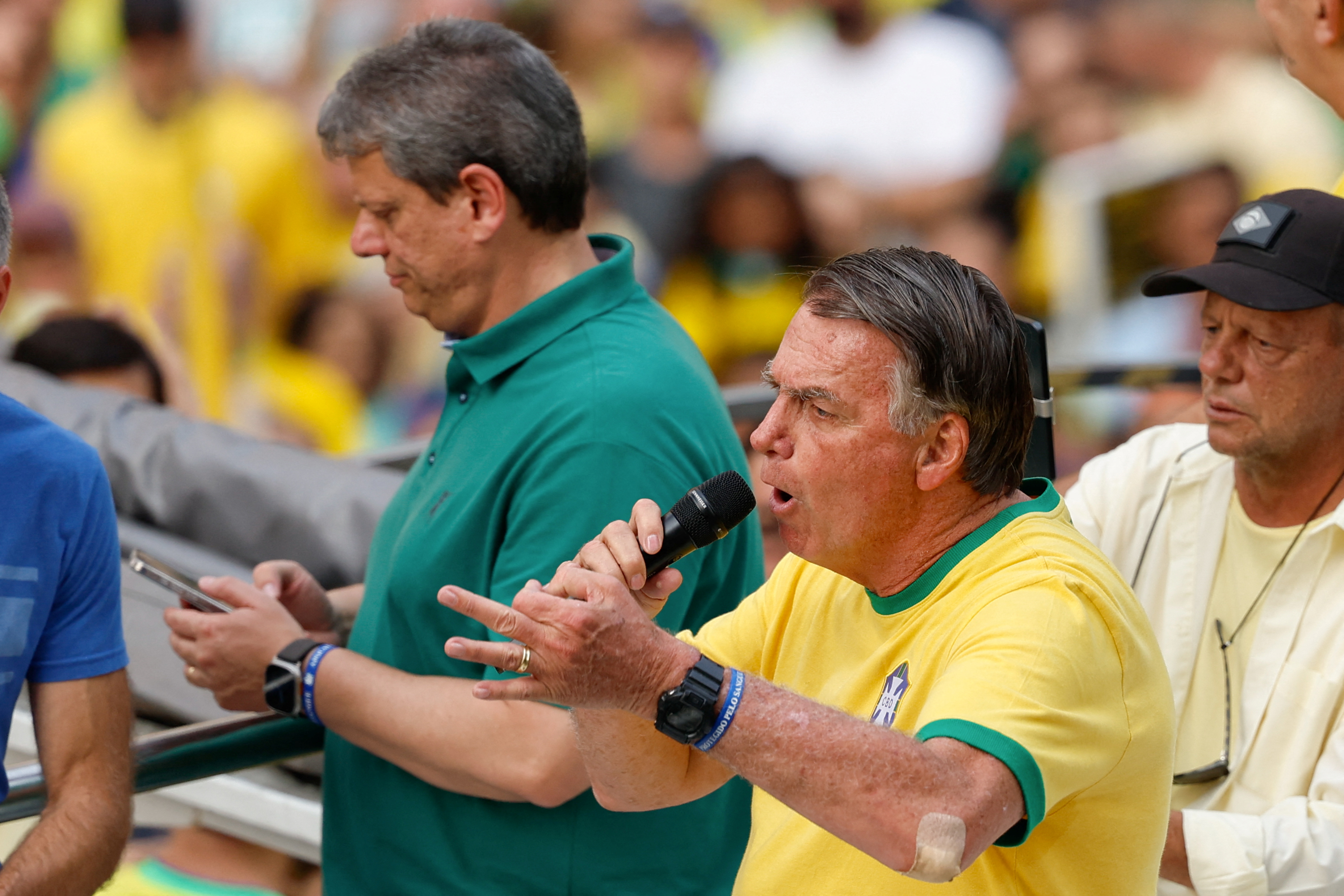 Jair Bolsonaro, in a yellow and green Brazil shirt, speaks to the crowd through a handheld microphone.