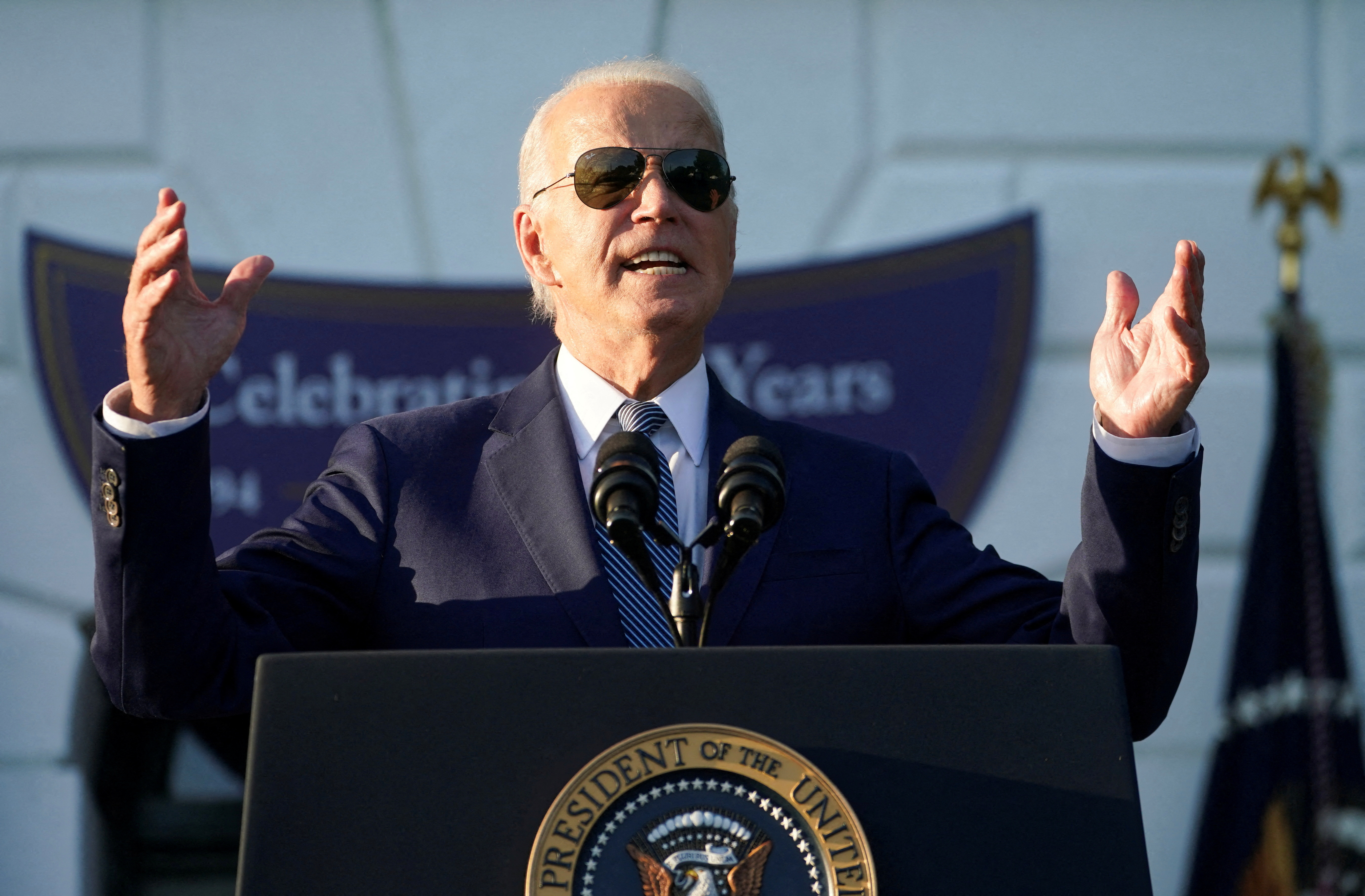 Joe Biden raises both arms as he speaks, wearing his signature aviator glasses.