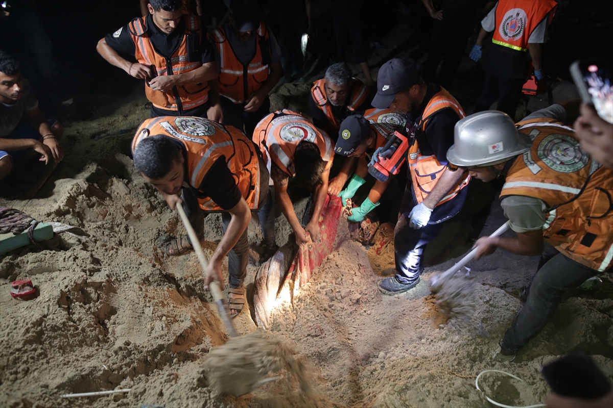 People in orange vests search a destroyed tent camp at night