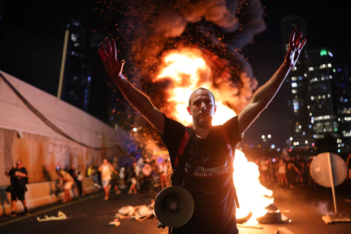A man raises his arms in front of burning wooden pallets as protesters block Tel Aviv's Ayalon highway