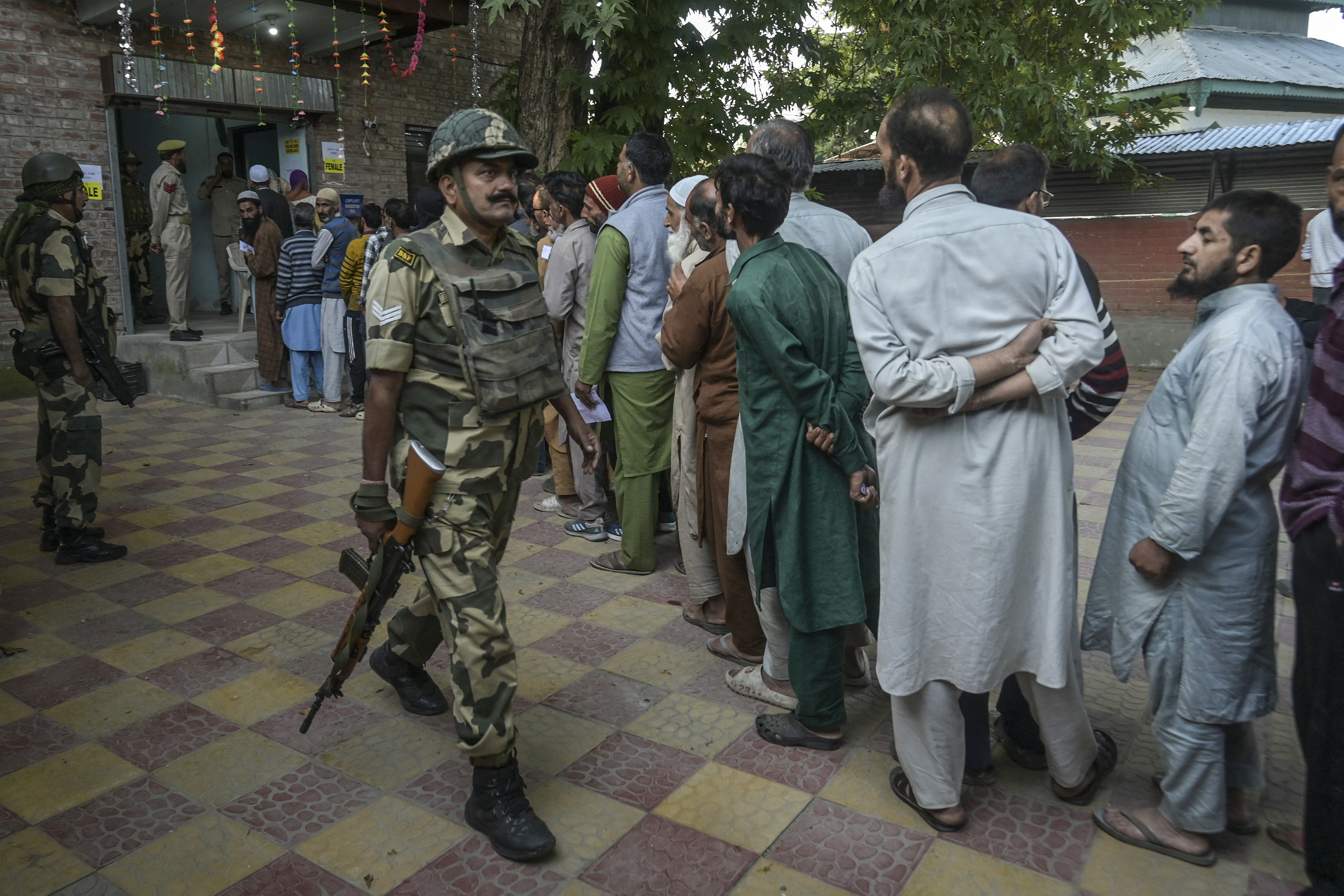 Indian security personnel stand guard as voters queue up to cast their ballots at a polling station during the first phase of assembly elections in Pulwama, south of Srinagar on September 18, 2024. - Indian-administered Kashmir began voting on September 18 in the first local elections since the cancellation of its special semi-autonomous status sparked fury in the troubled Himalayan territory, which is also claimed by Pakistan. (Photo by TAUSEEF MUSTAFA / AFP)