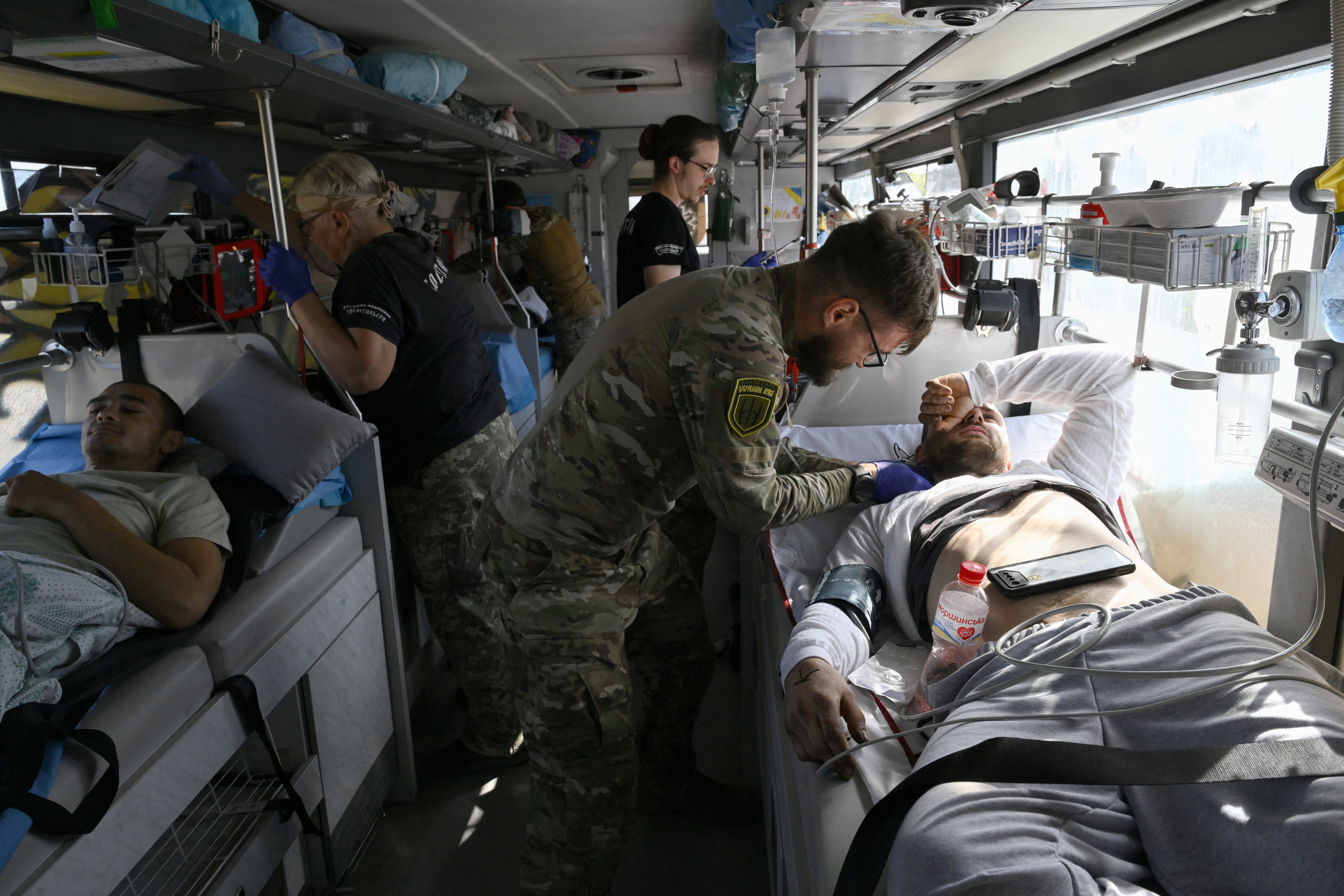 Ukrainian soldiers receiving medical treatment. They are lying in beds in a special evacuation bus. A paramedic is attending to one of the soldiers.