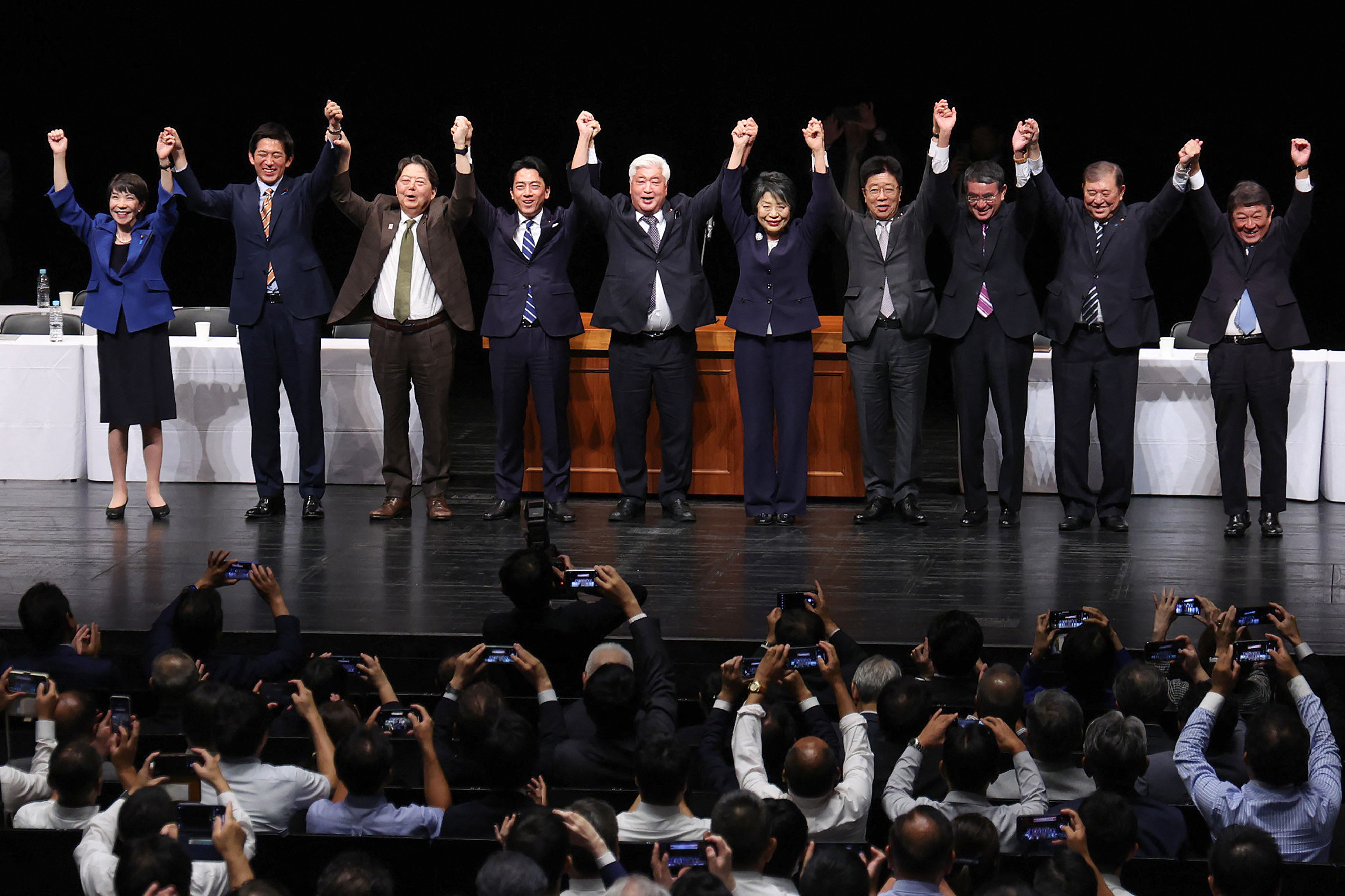 Some of the candidates for the LDP leadership contest. There are two women and the rest are men. They are standing in a line and holding their hands in the air