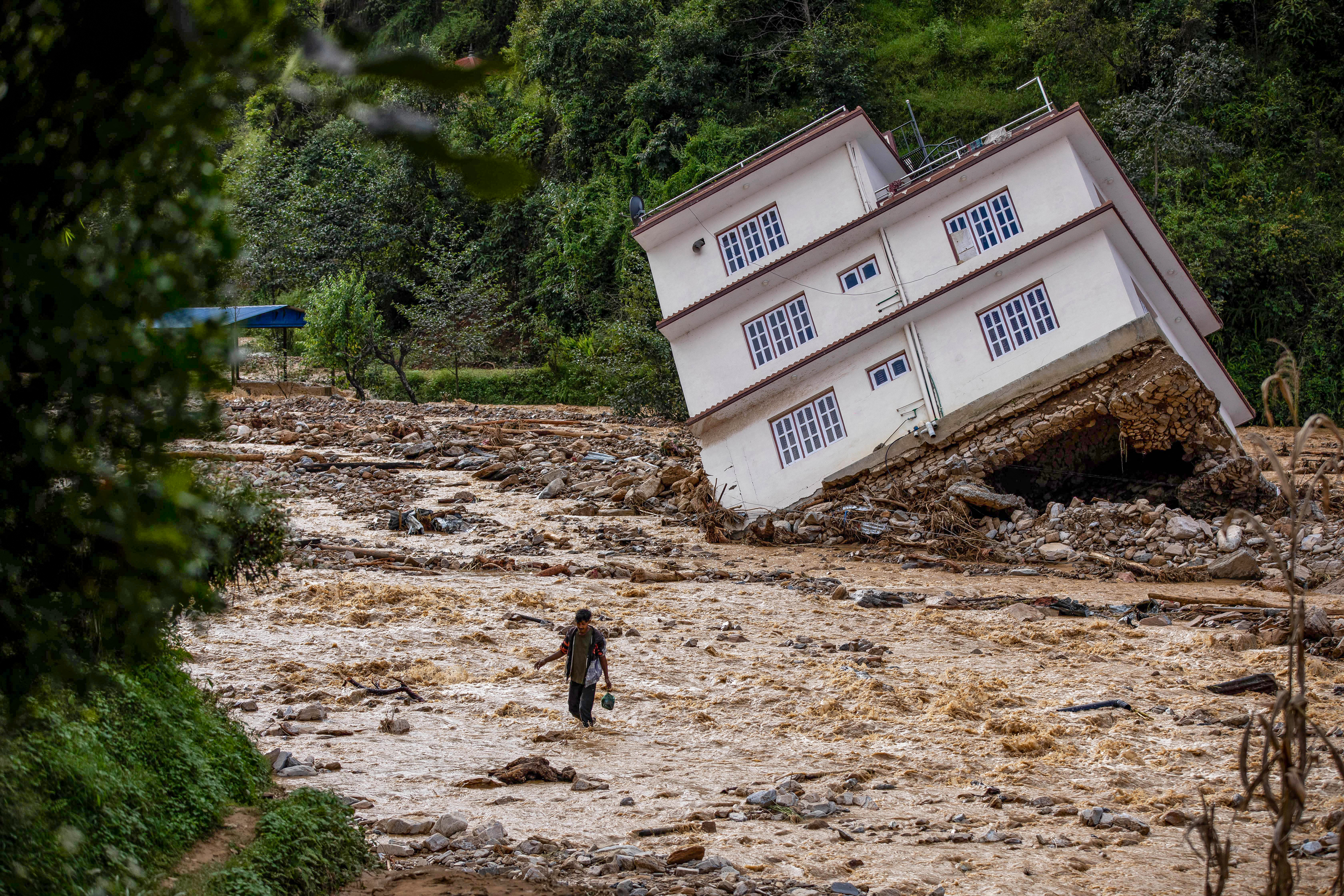 A man wades through the flood waters in the affected area of monsoon flooding in Roshi village of Nepal's Kavre district on September 30, 2024.