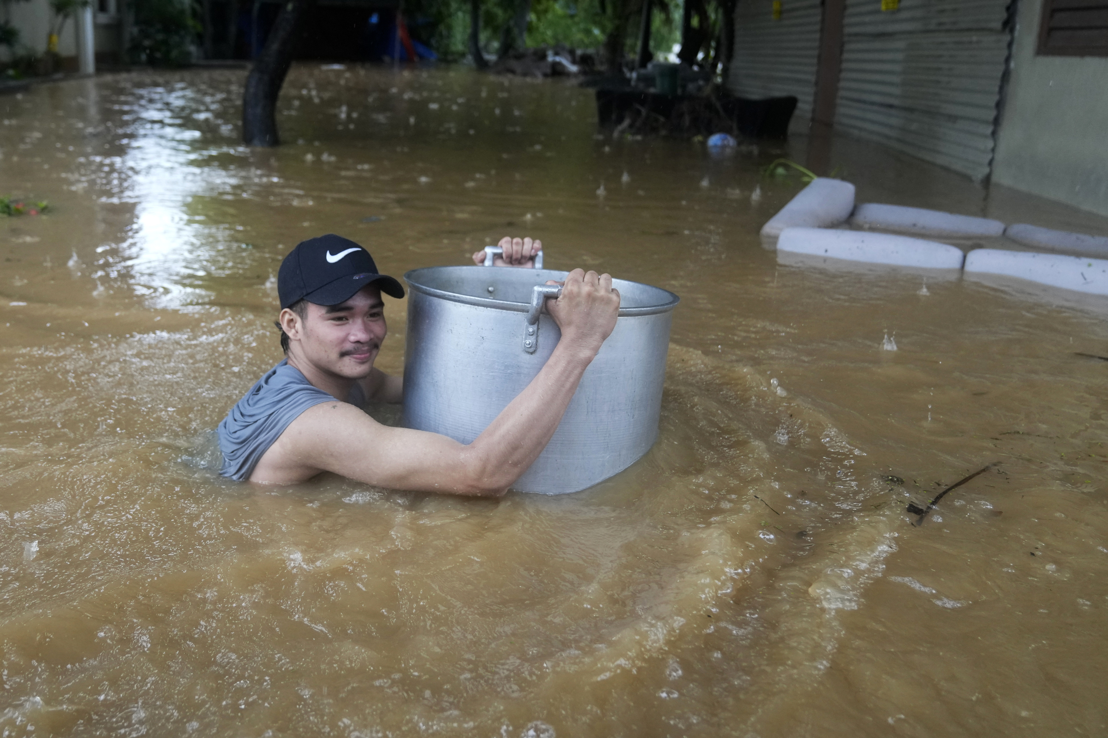 A resident uses a large pot to keep him afloat as he negotiates a flooded street caused by heavy rains from Tropical Storm Yagi,
