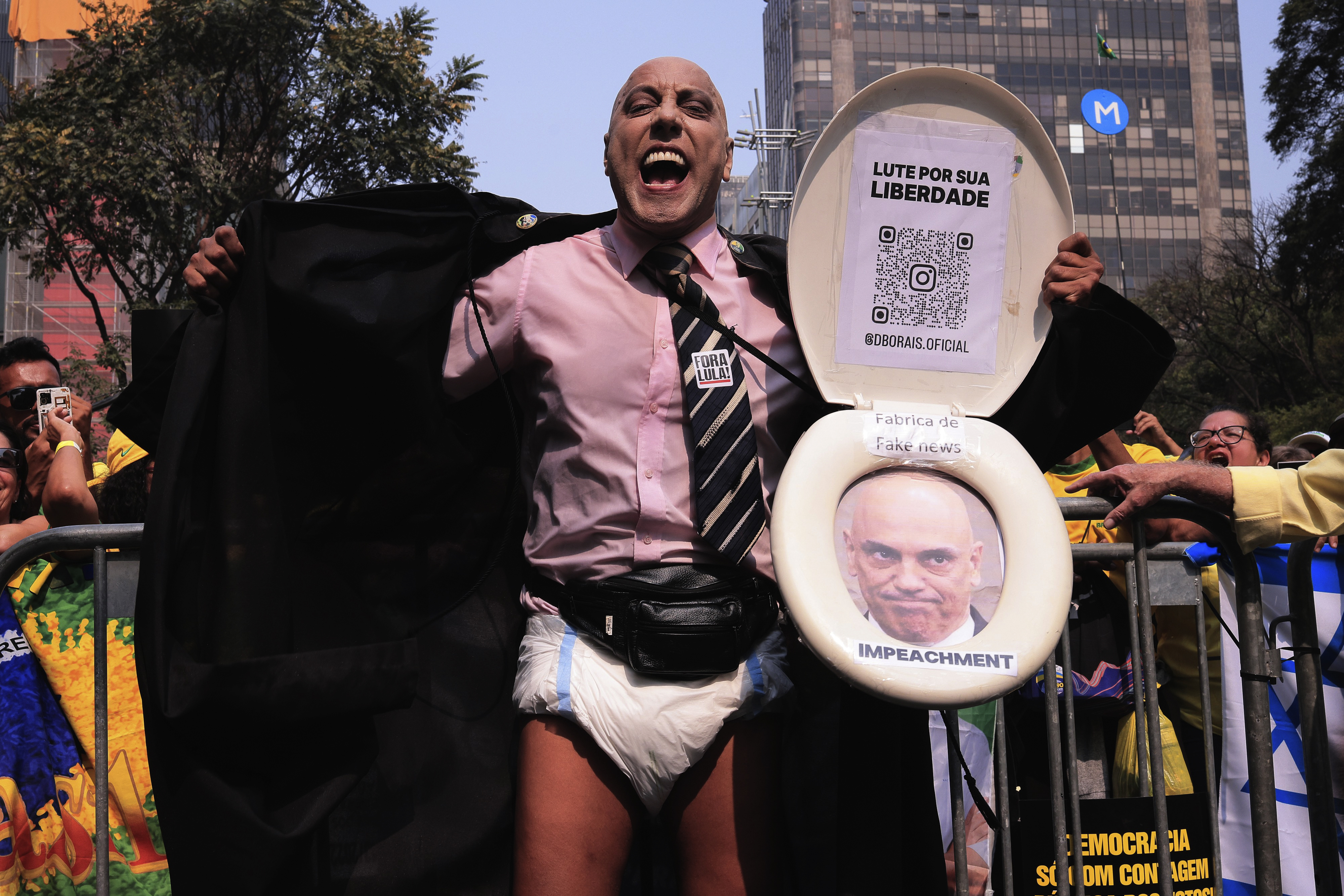 A protester is dressed in a diaper, a dress shirt and tie. He holds up a toilet seat with Alexandre de Moraes's face inside.