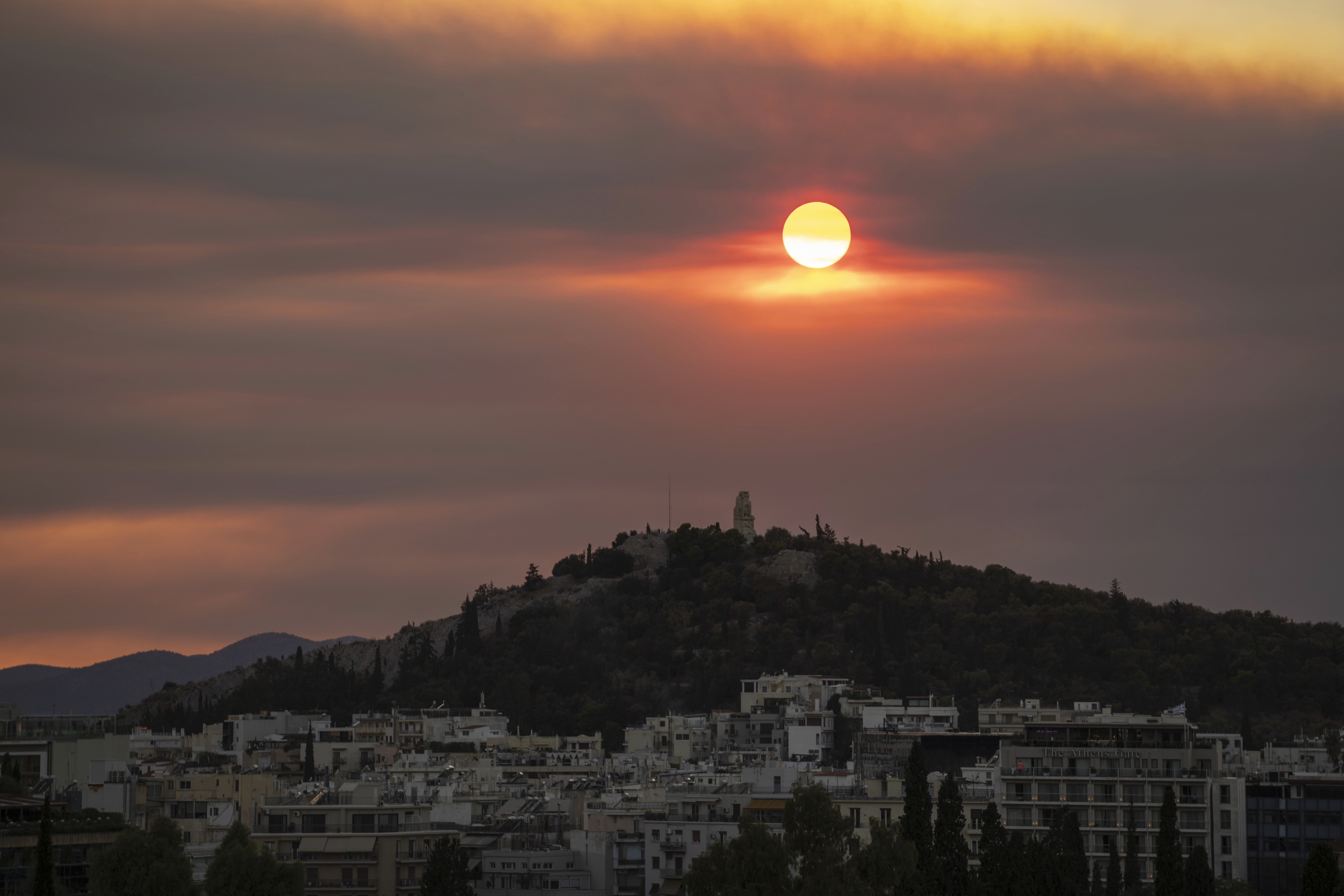 The sun sets behind the Philopappos hill as smoke from a wildfire which is located some 150 kilometers (93 miles) southwest of Athens, covers the sky over the western suburbs of Greece's capital, Monday, Sept. 30